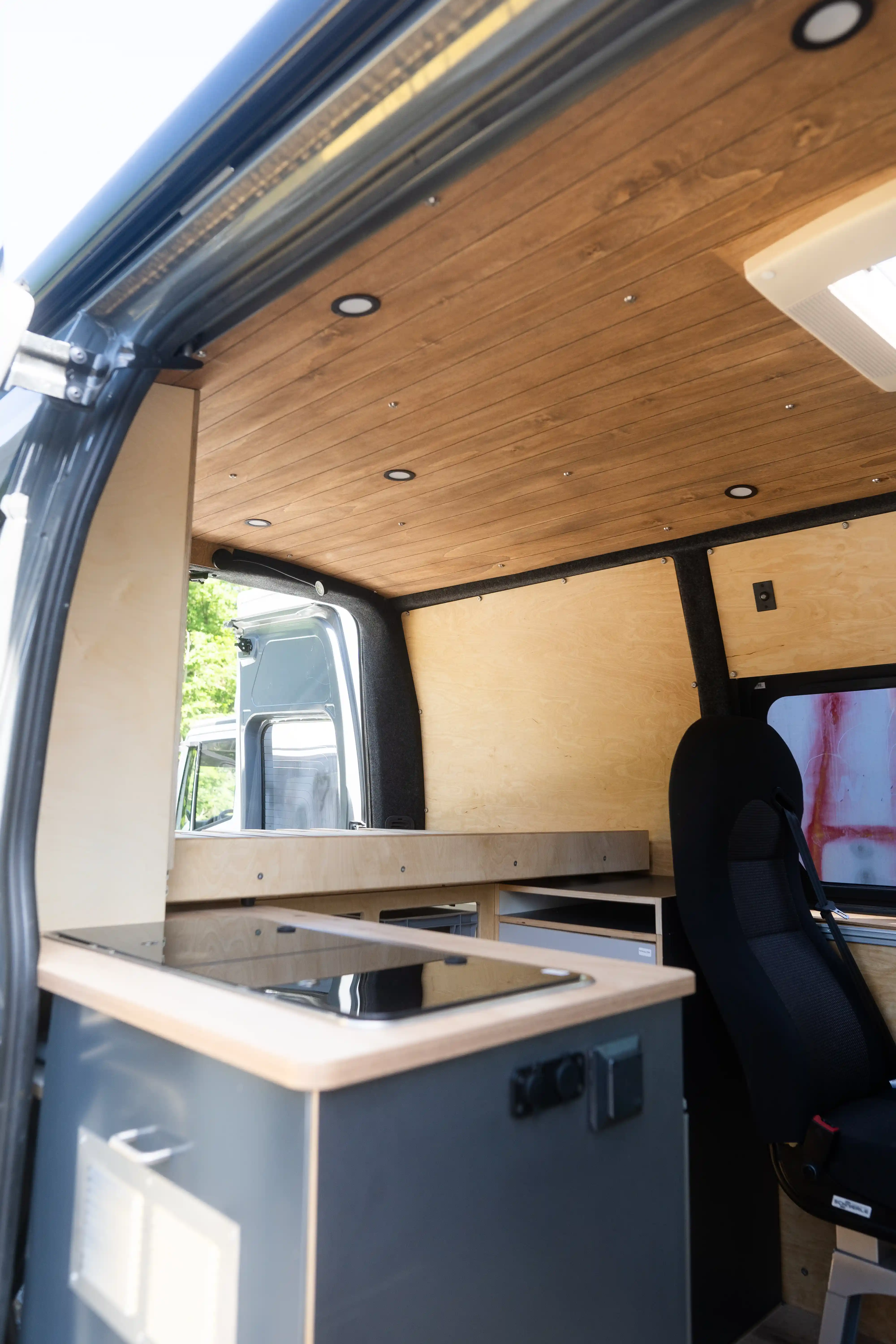 Gesamtansicht des Renault Master Camper-Ausbaus durch die geöffnete Schiebetür, zeigt Wandverkleidungen aus Multiplex, Dachhimmel aus Pappelsperrholz und Kleiderschrank mit Schiebetüren