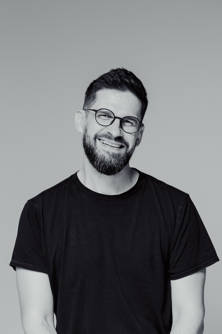 Bartłomiej Zylla uśmiechnięty w czarnym t-shircie i okularach