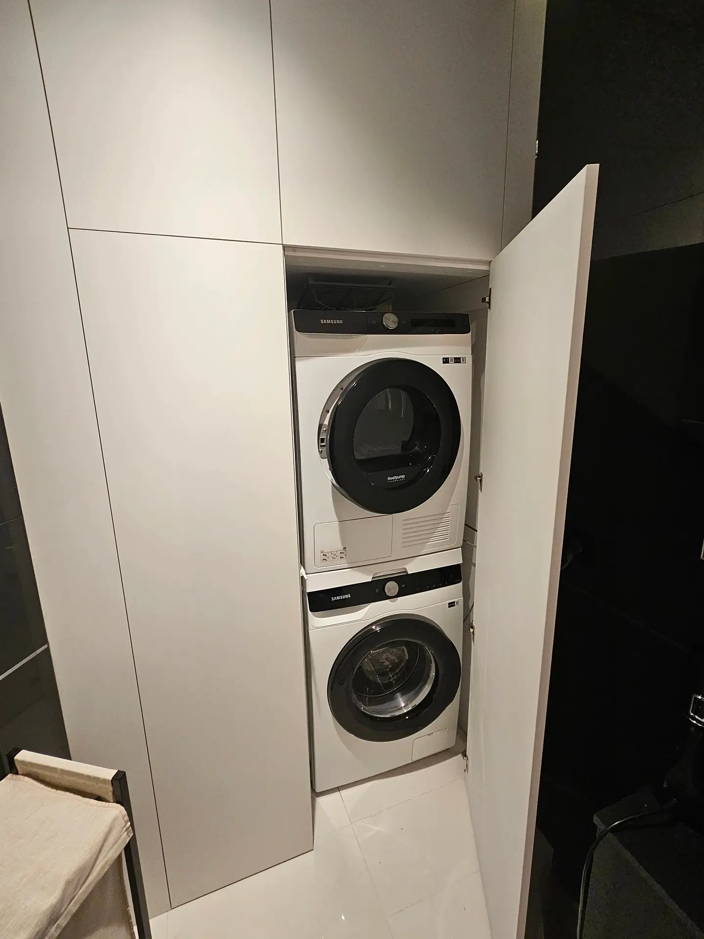 Funkcjonalna szafa wnękowa w łazience z otwartymi drzwiami, kryjąca pralkę i suszarkę w słupku.