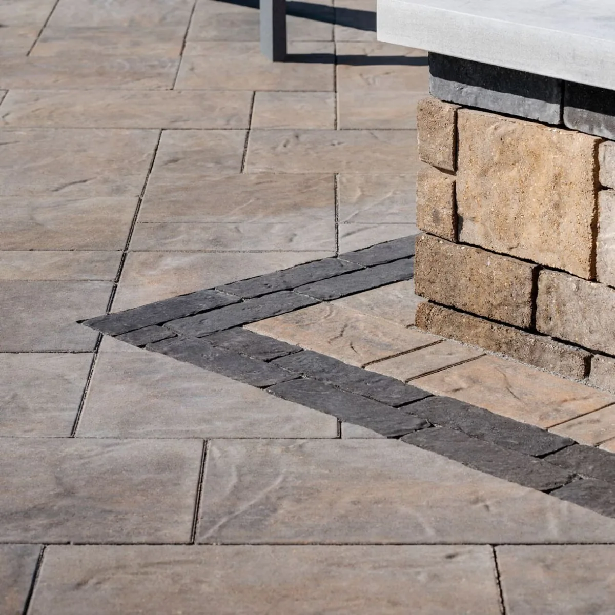 Light rectangular paving with a contrasting dark border beside a stone-faced outdoor counter.