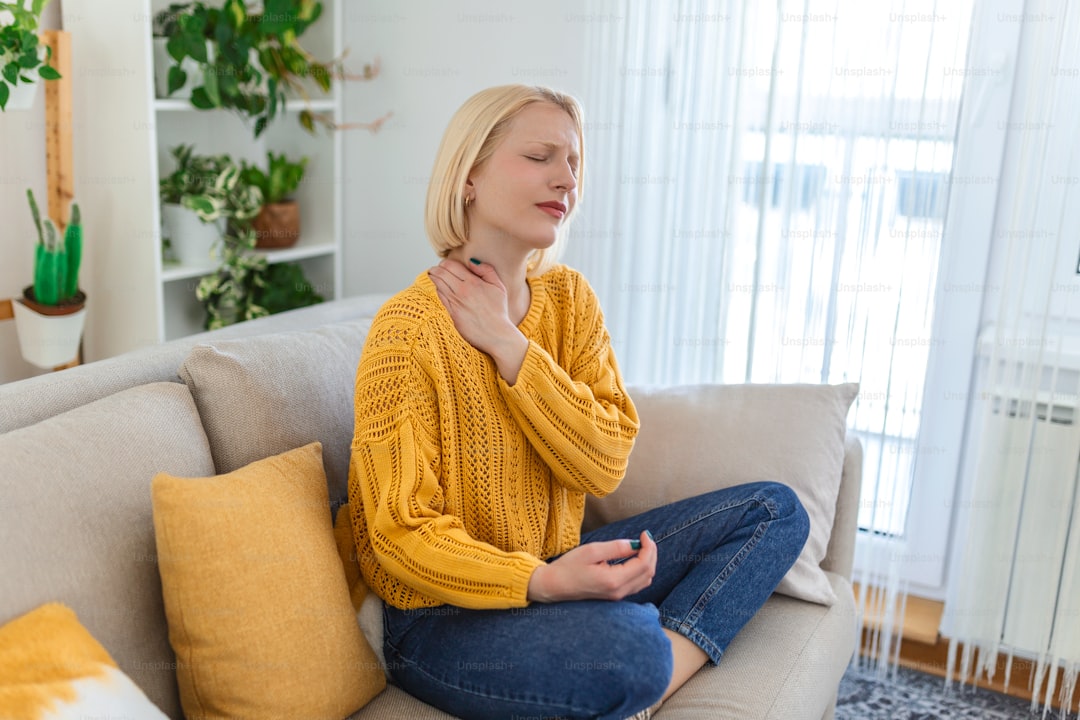 Femme souffrant de douleur au cou assise sur un canapé, mode détente intérieure.