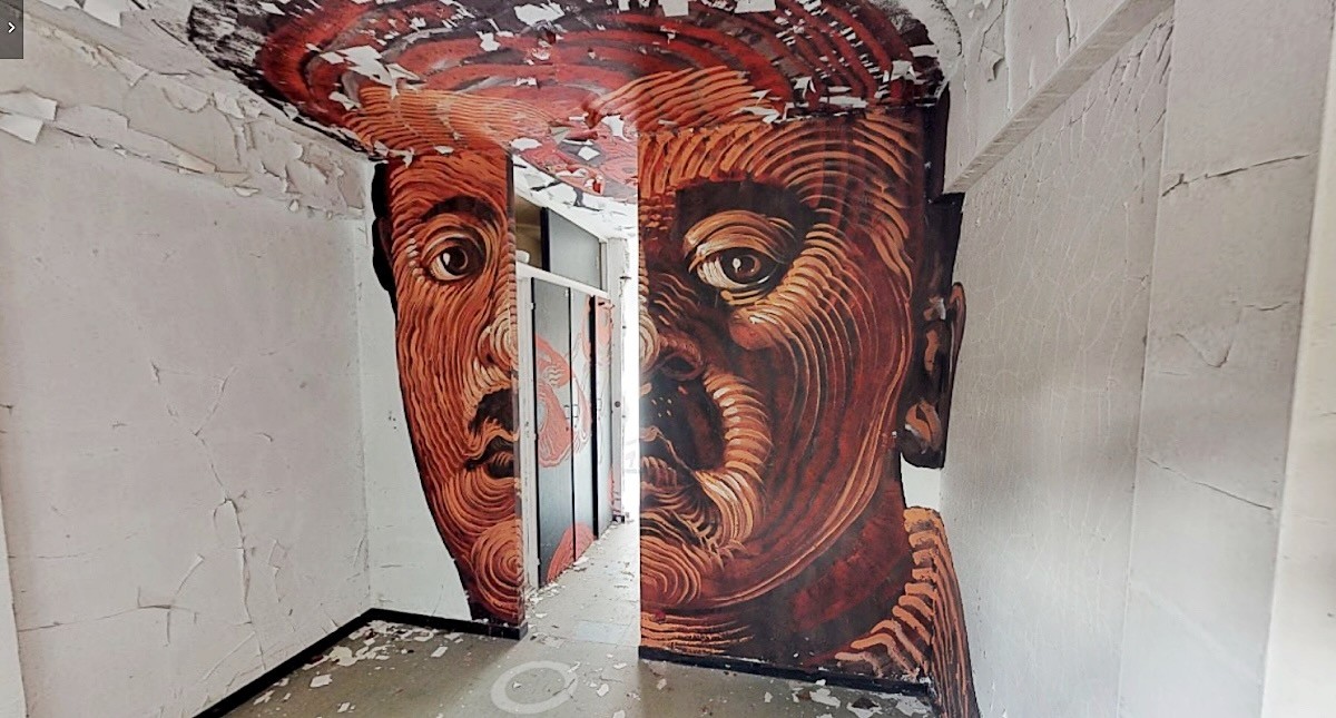 A face painted in red-brown ridges spans the corner of a crumbling room.