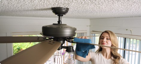 A hand wiping the top surface of a ceiling fan blade clean.