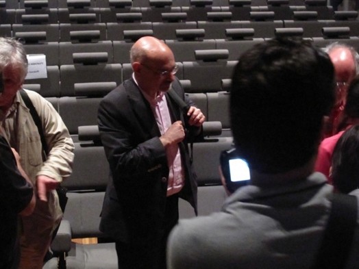 A photo of a man in a suit sitting in a cinema.