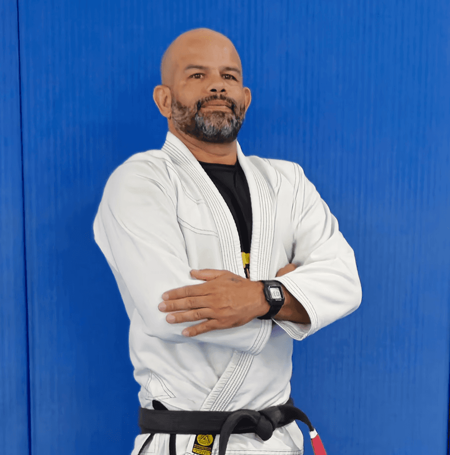 Tony “Ourico” in a white gi, arms crossed, standing confidently in front of a blue background