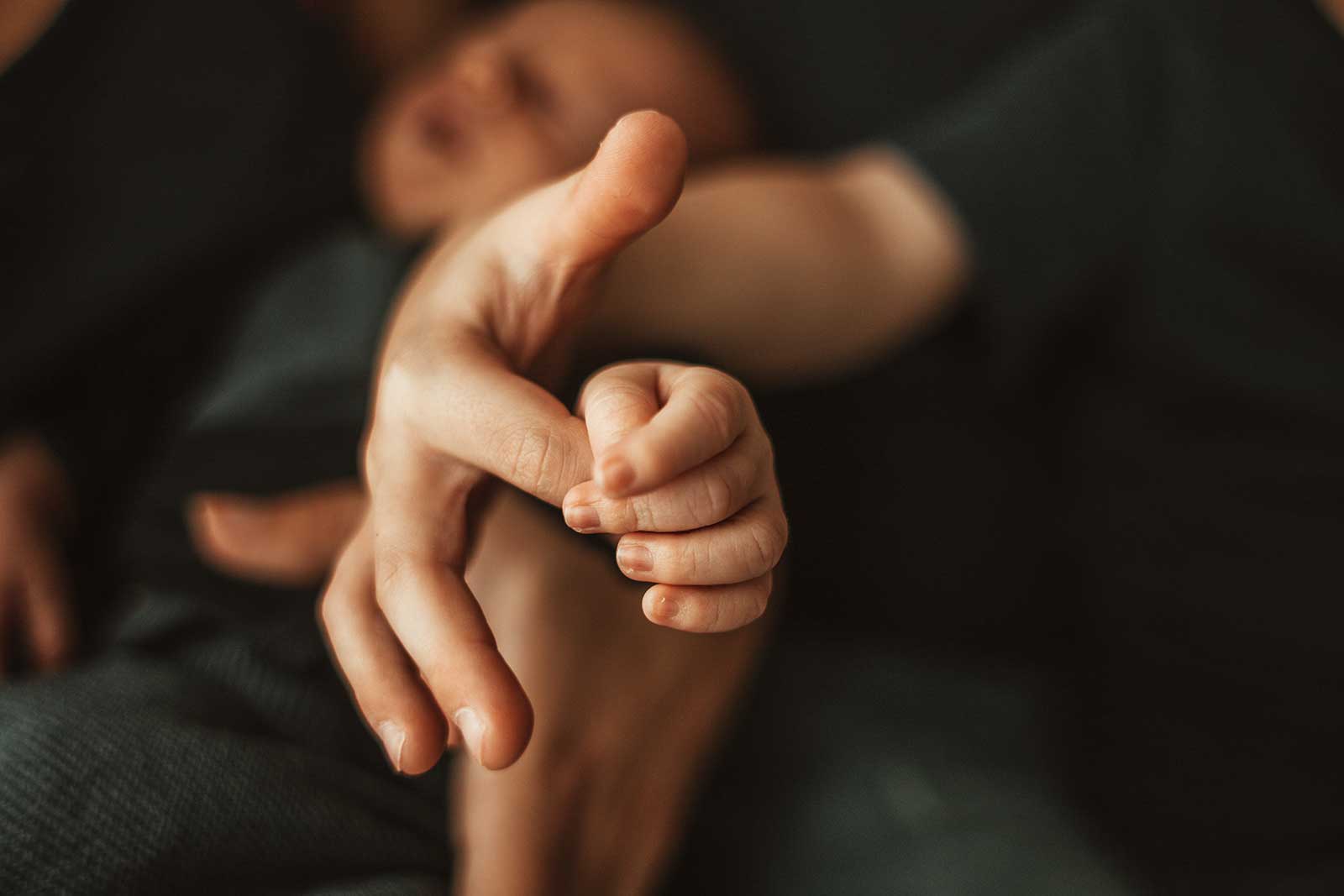 Eine kleine Babyhand hält einen Finger der Mutter