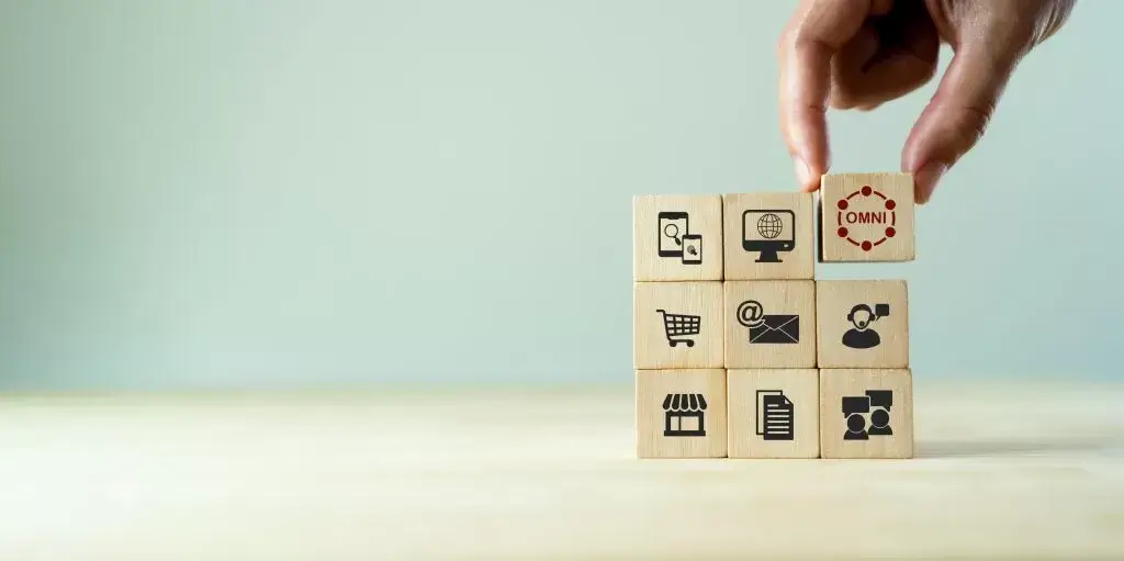 Image showing a stack 3x3 of wood cubes with common business icons on each. A hand is placing a final cube in the to right with a red omni icon on it