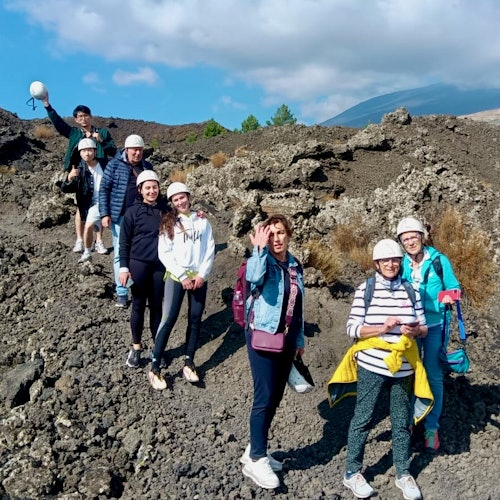 Um grupo de sete pessoas usando capacetes e roupas de exterior está de pé em um terreno rochoso sob um céu parcialmente nublado.