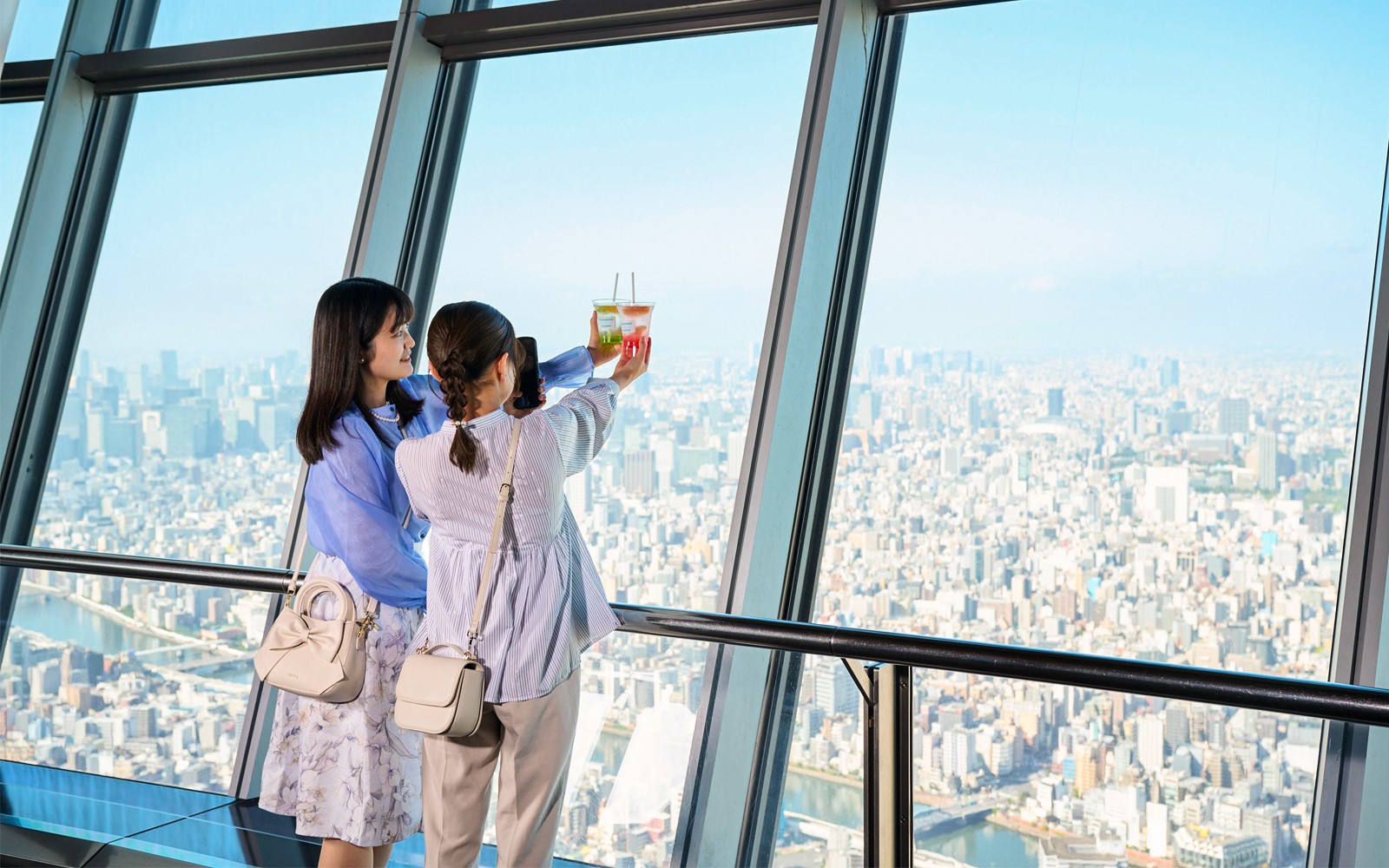 Tourists on Tokyo's Tembo Deck enjoying city views with soft drinks.
