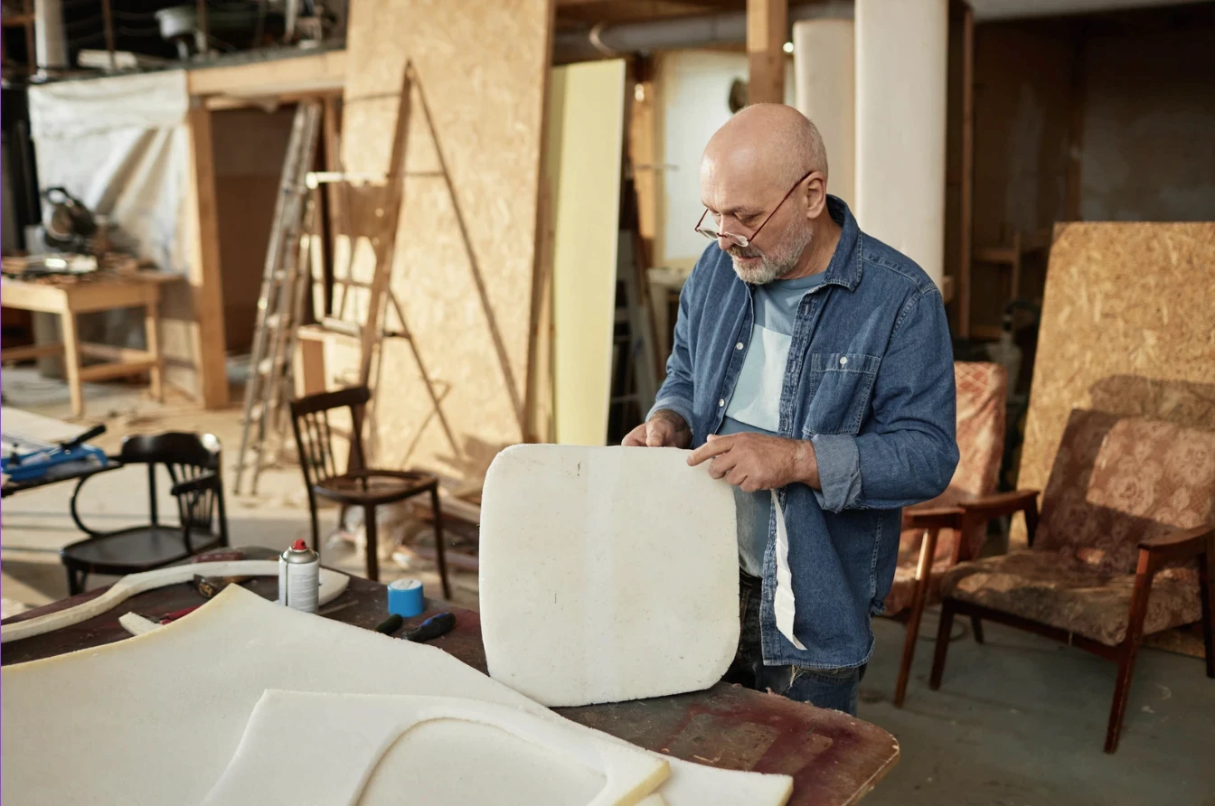 Man working on furniture upholstery in carpentry workshop with tools and chairs