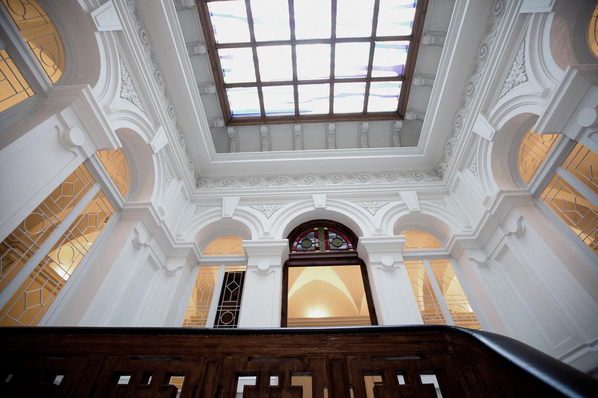 Perspektivische Aufnahme von einer prächtigen Decke mit Glasfenster und architektonischen Details, darunter Bögen und Holzarbeiten.