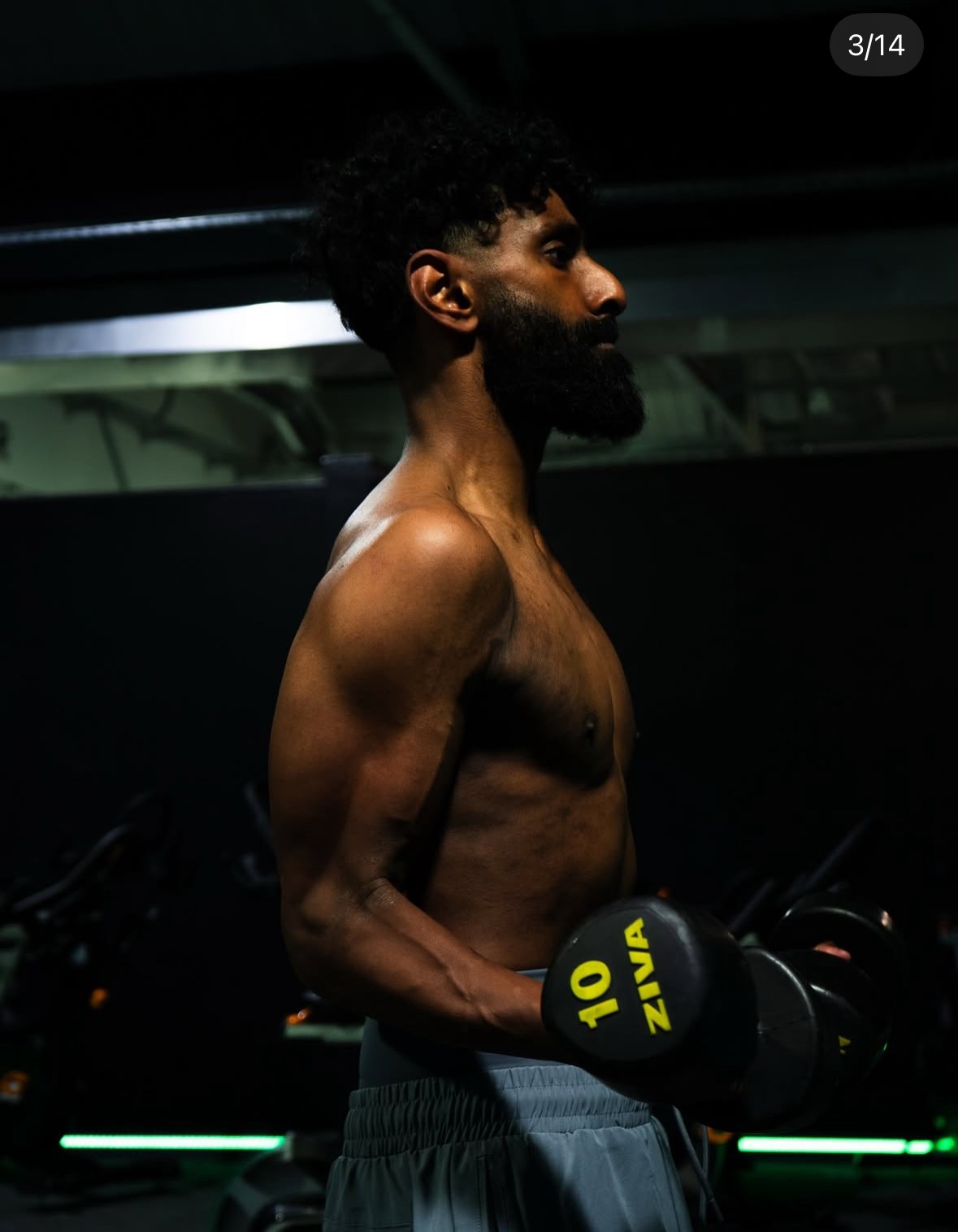 Male athlete performing a bicep curl with 10kg dumbbells in a dark fitness studio.