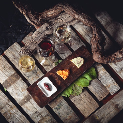 Two glasses of white wine, one of red, cheese, and chocolate on a wooden board set on a rustic wooden surface with vines.