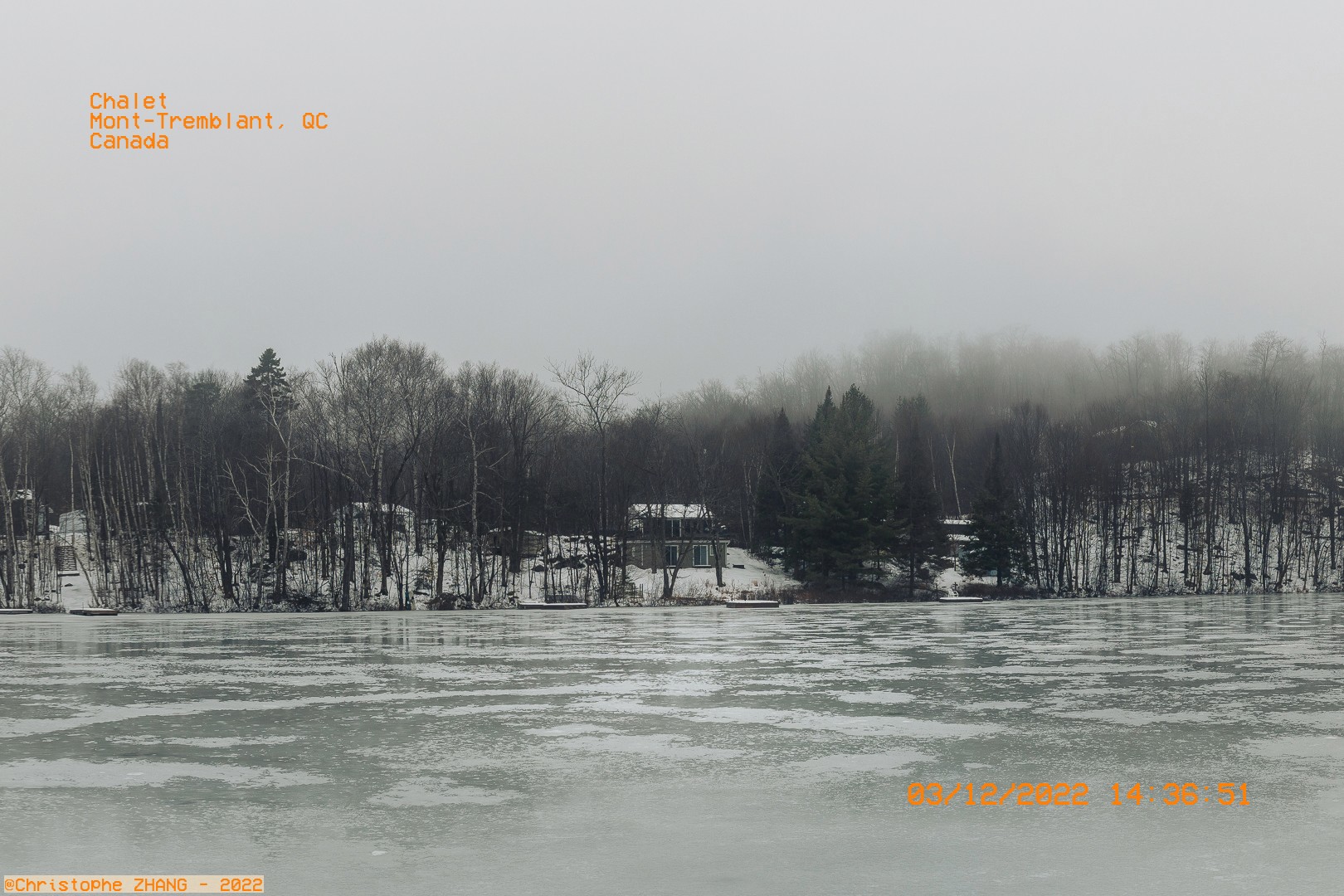 Scène brumeuse à Mont-Tremblant avec un chalet isolé en hiver près d’un lac gelé