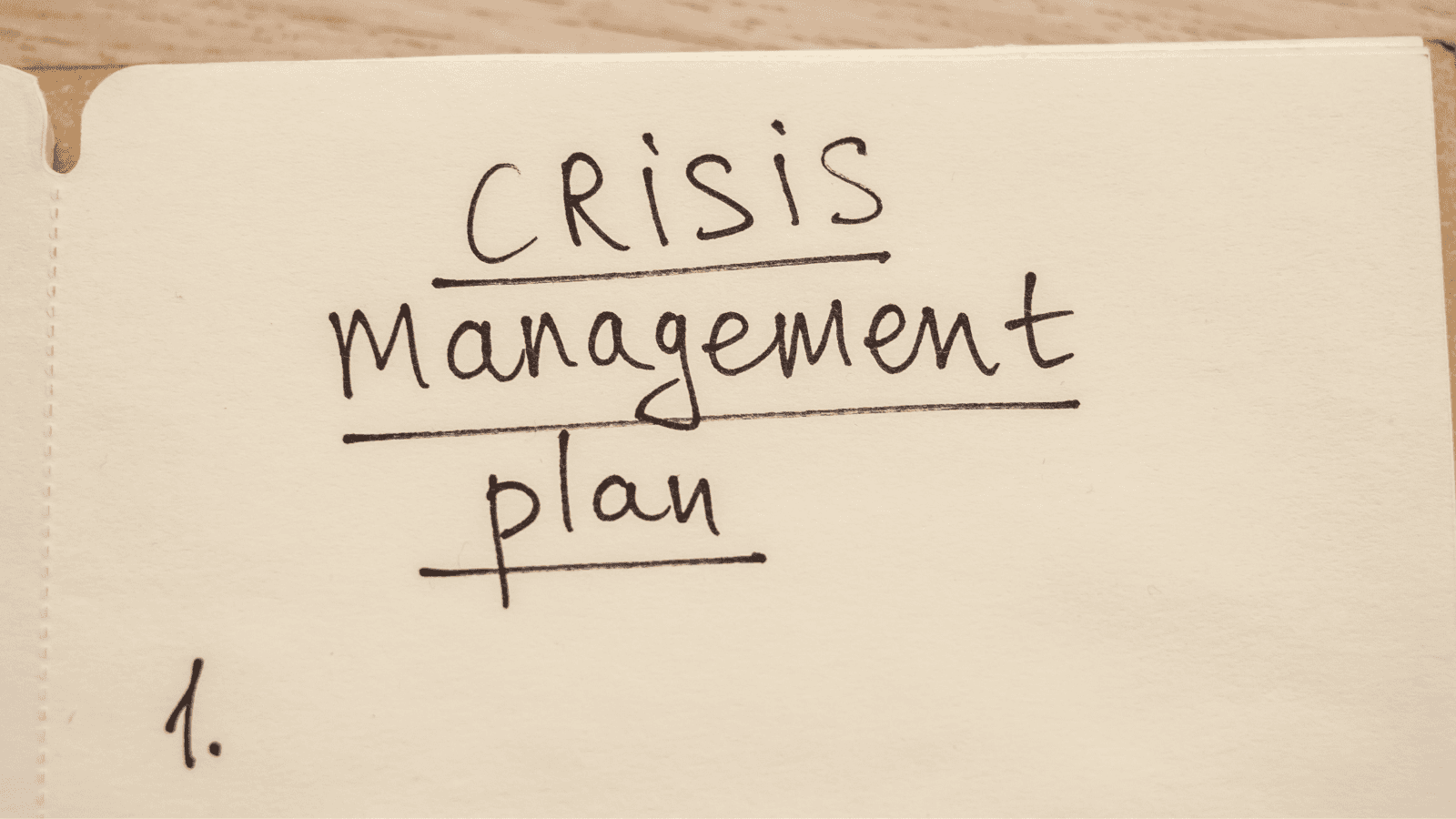 A manilla folder with the words "Crisis Management Plan" and the number 1 handwritten and underlined on it in underlined 