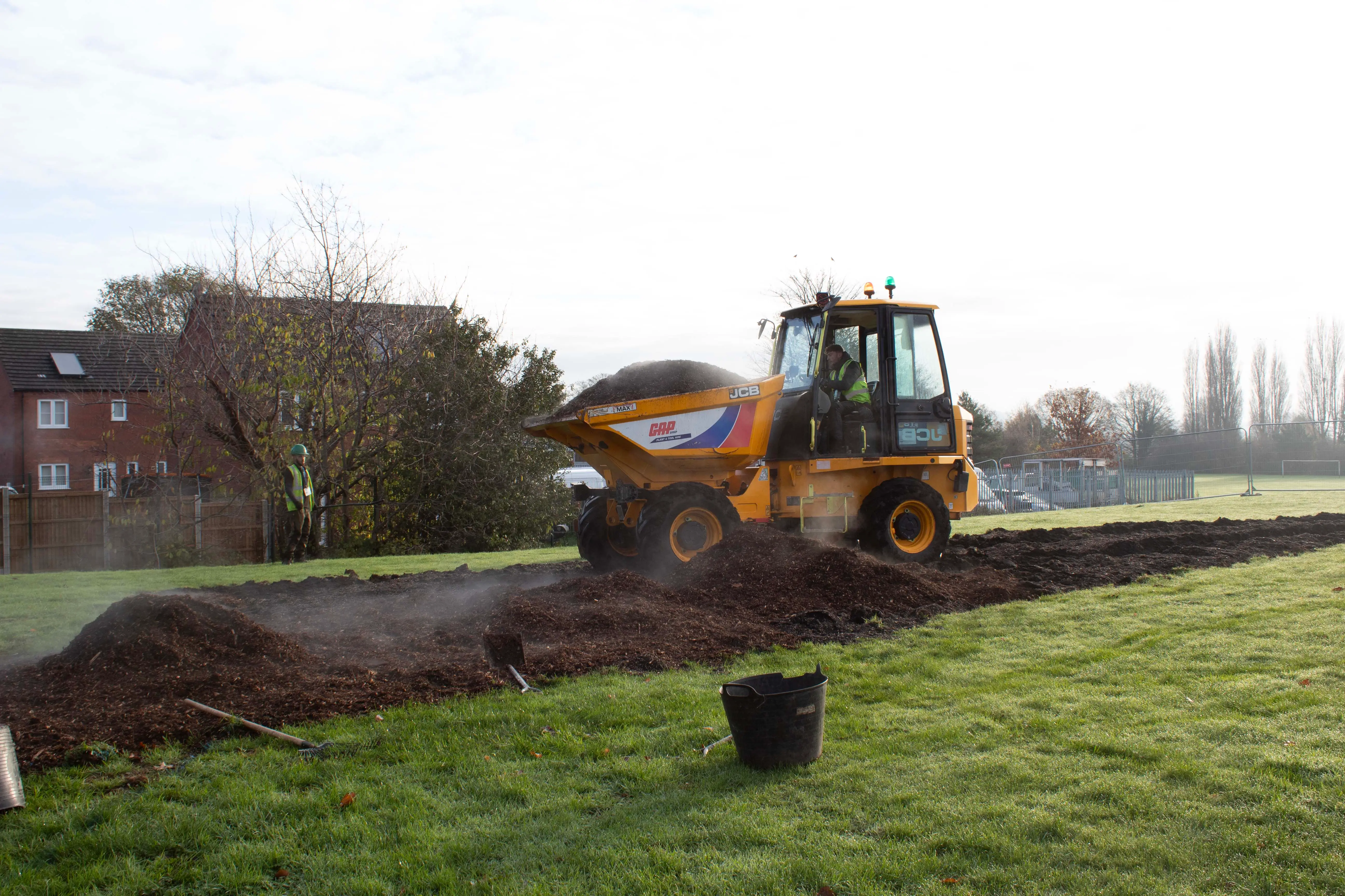 A large construction vehicle dump truck is loading material on a grassy area under a cloudy sky.