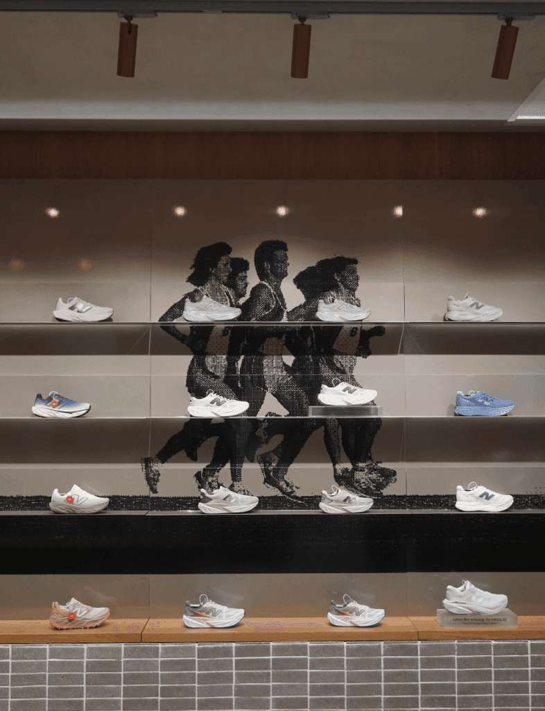 A display showcasing various New Balance running shoes on shelves, with a stylized mural of runners in motion as the backdrop.