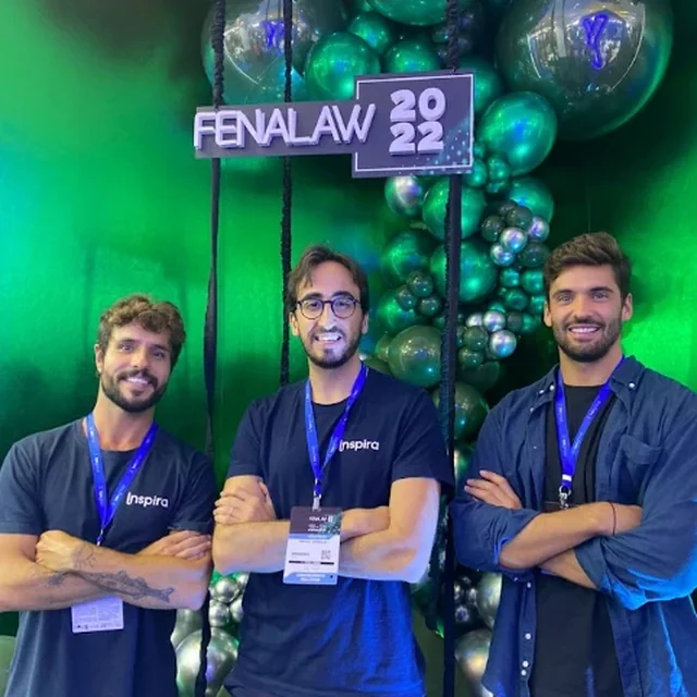 Três integrantes do time da Inspira, de camiseta da empresa e crachá, diante do letreiro da Fenalaw 2022