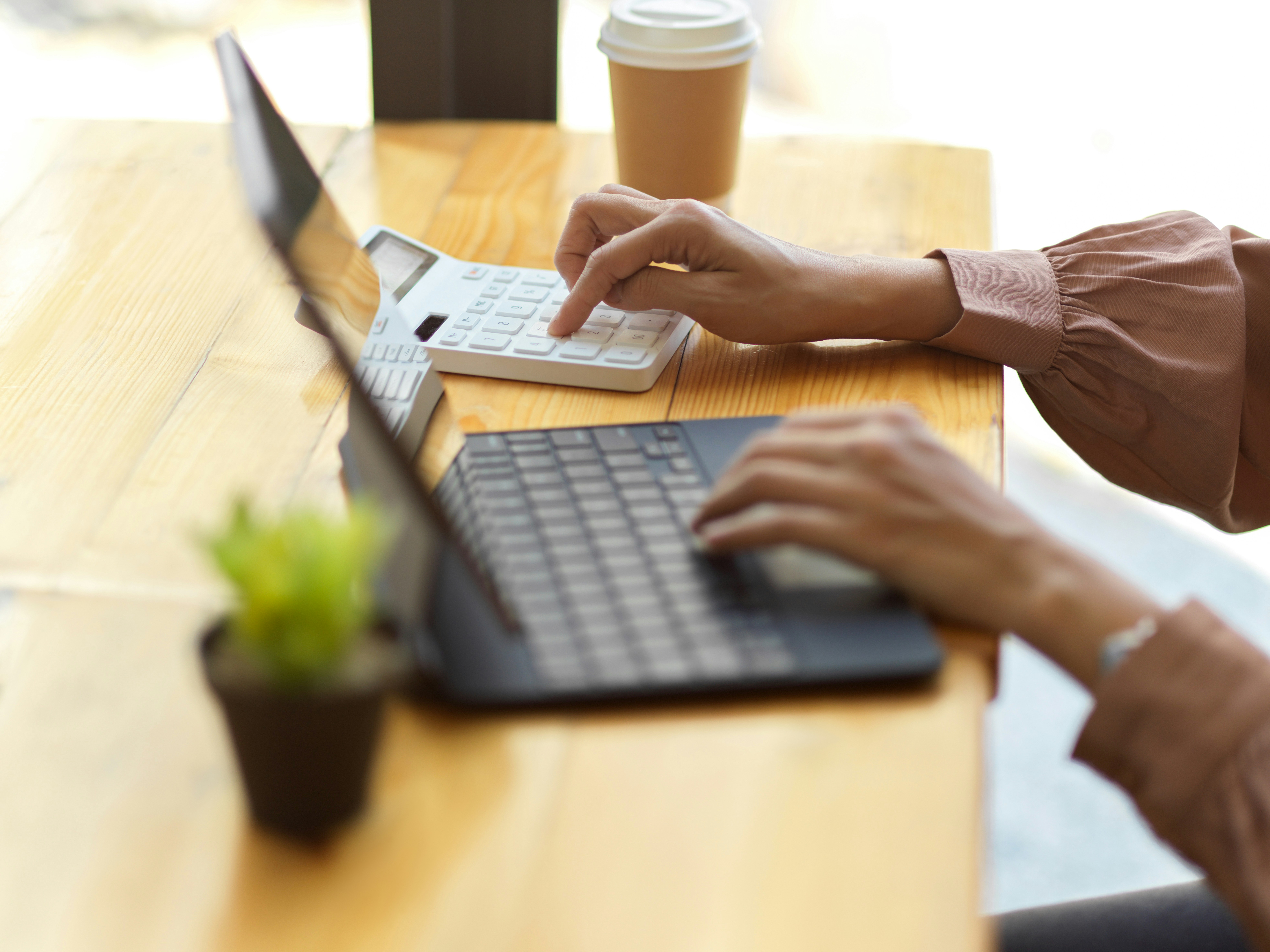 Osoba wykonująca obliczenia księgowe przy laptopie i kalkulatorze