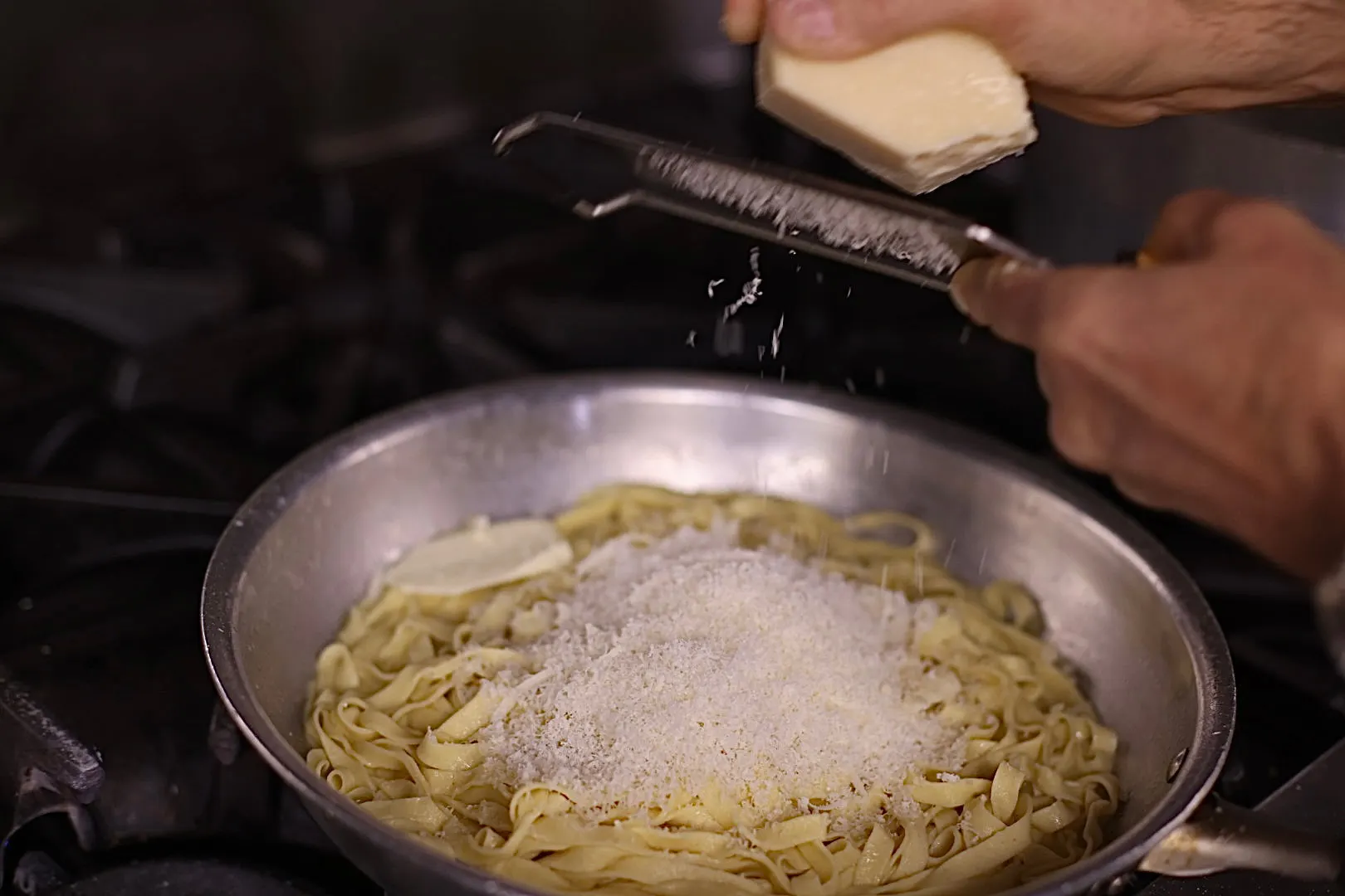 Fresh pasta in a pan with cheese being grated over it