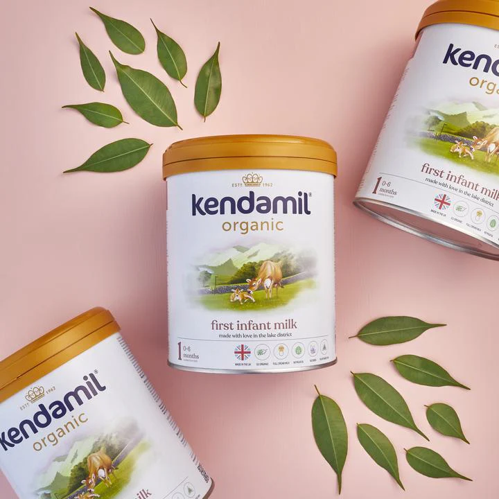 Three jars of a product arranged on a pink background, surrounded by green leaves.