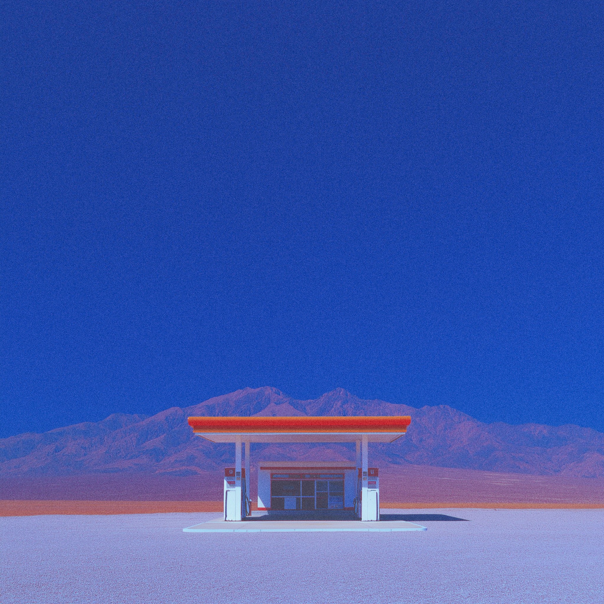 A solitary gas station stands in a flat desert with mountains behind it under a vast, intense blue sky.