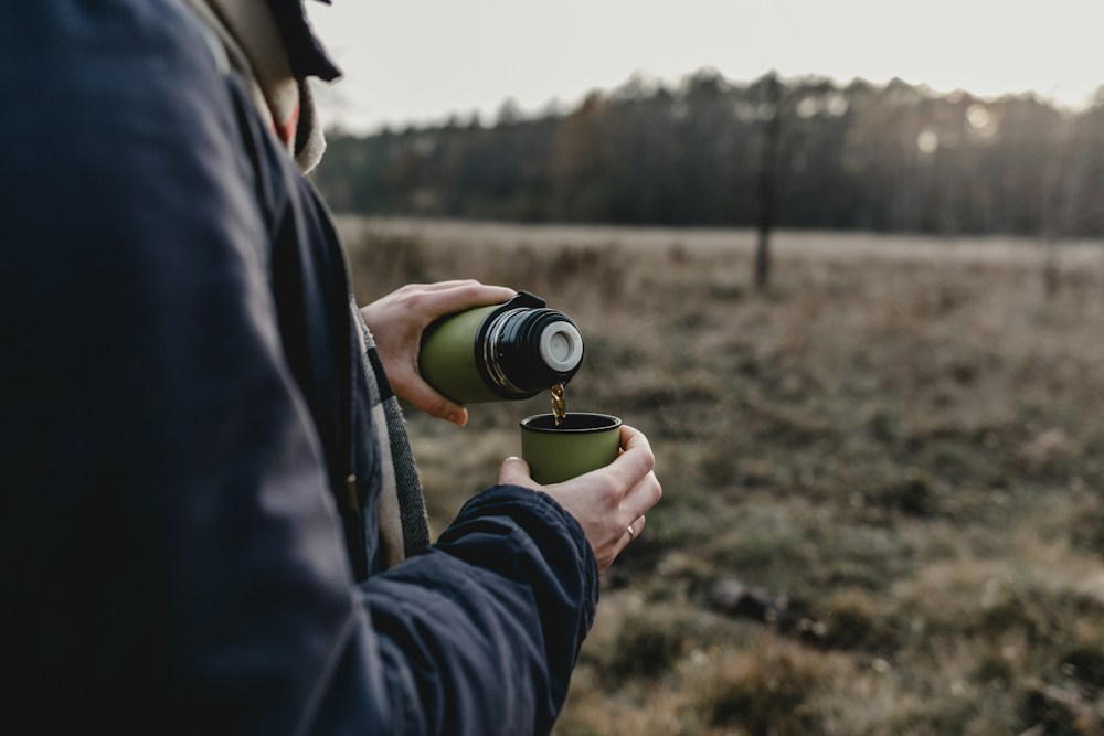 A walker pouring hot tea from a flask on an autumn moor