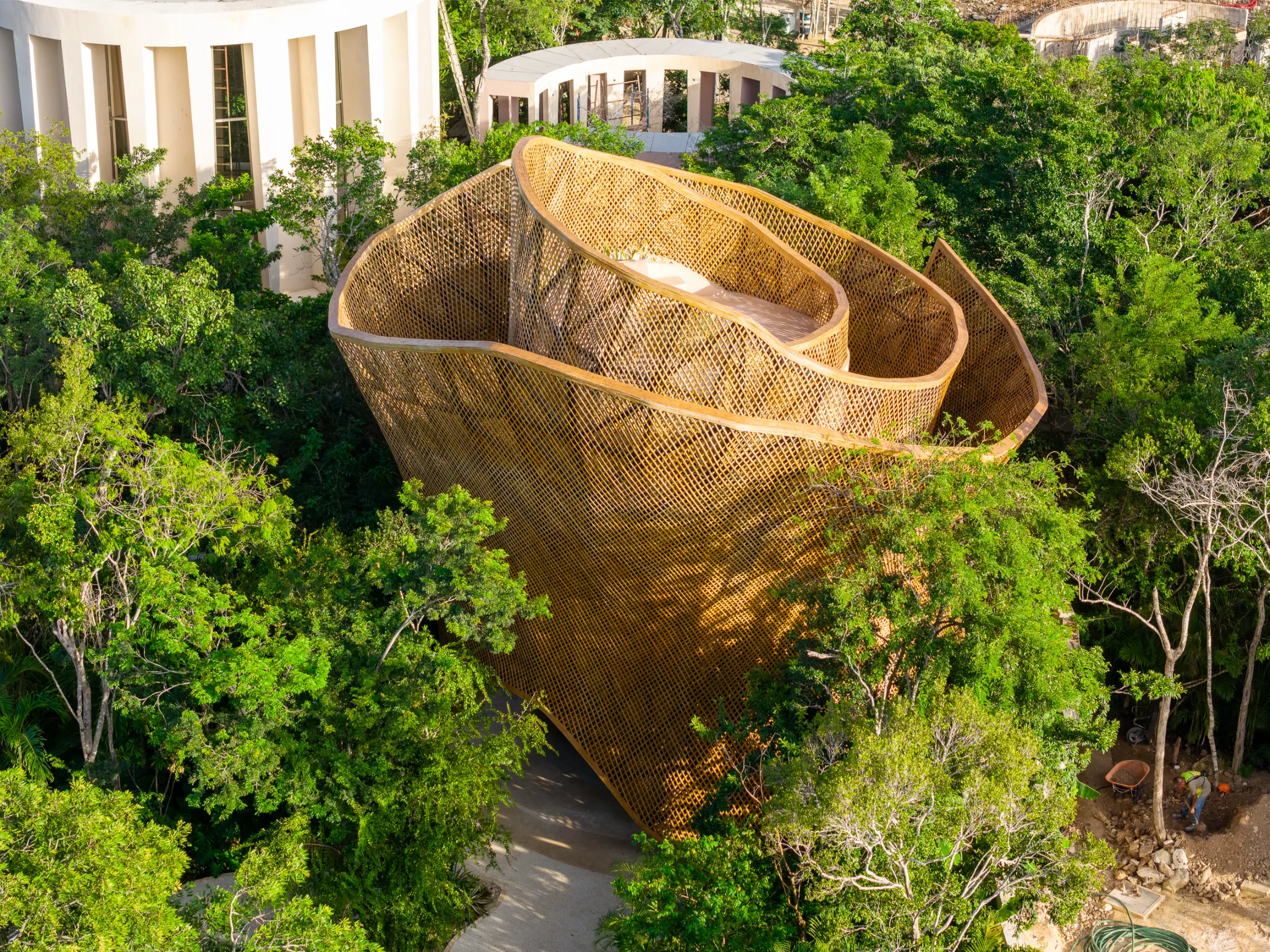 Exterior view of the Aflora reception tower in Tulum, featuring a monumental parametric bamboo skin that spirals upwards, seamlessly integrating with the surrounding jungle canopy.