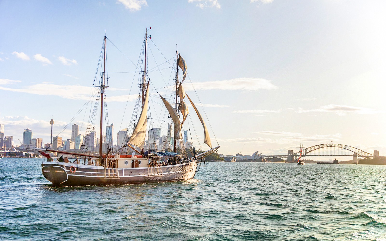 Paglalayag ng mataas na barko sa Sydney Harbour na may Harbour Bridge sa likuran.