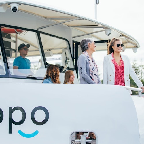 Several people standing on the deck of a boat with "Opo" visible on the side. Two women are smiling and talking.