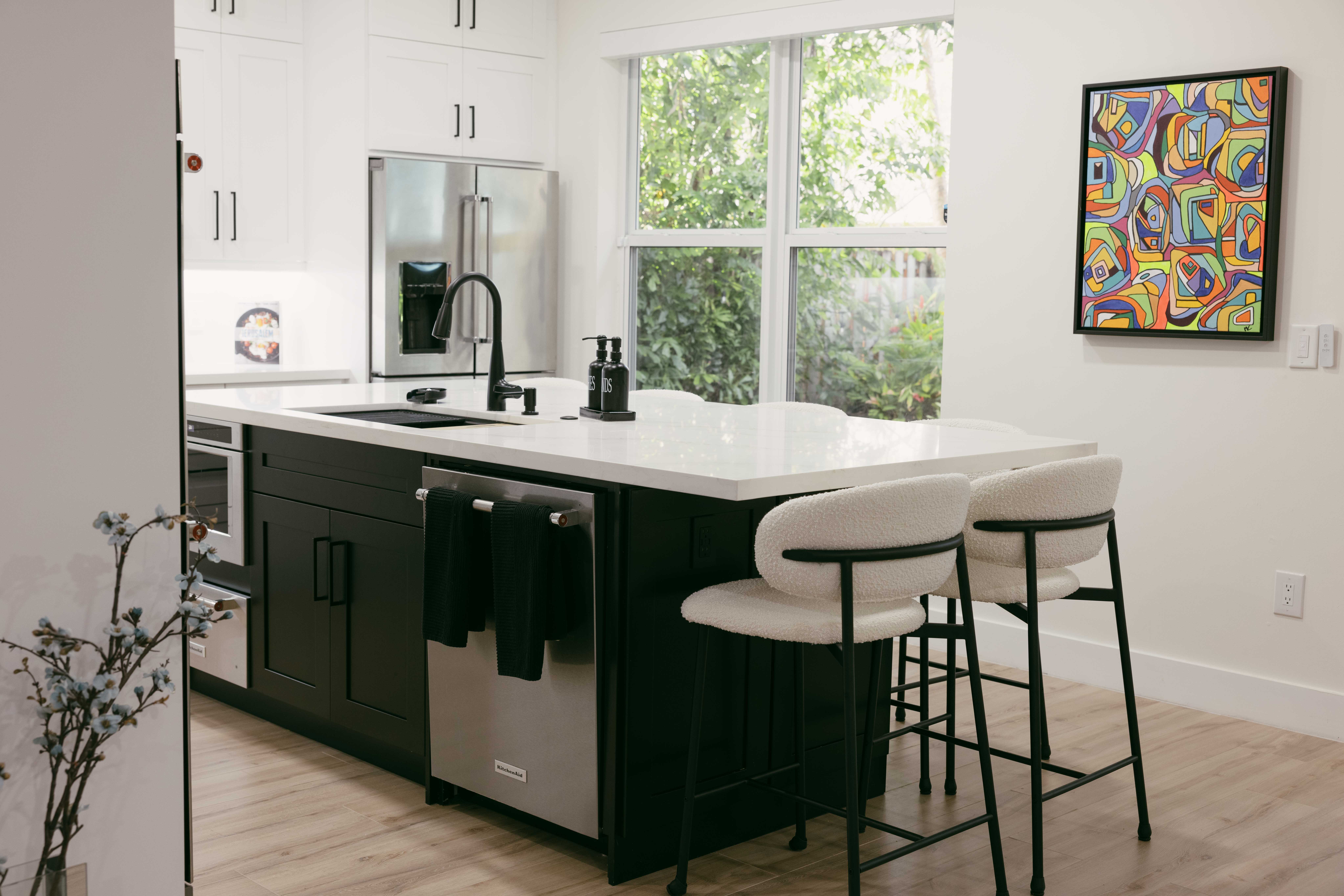 Modern kitchen with black island, white countertops, and stylish bar stools. Art on wall.