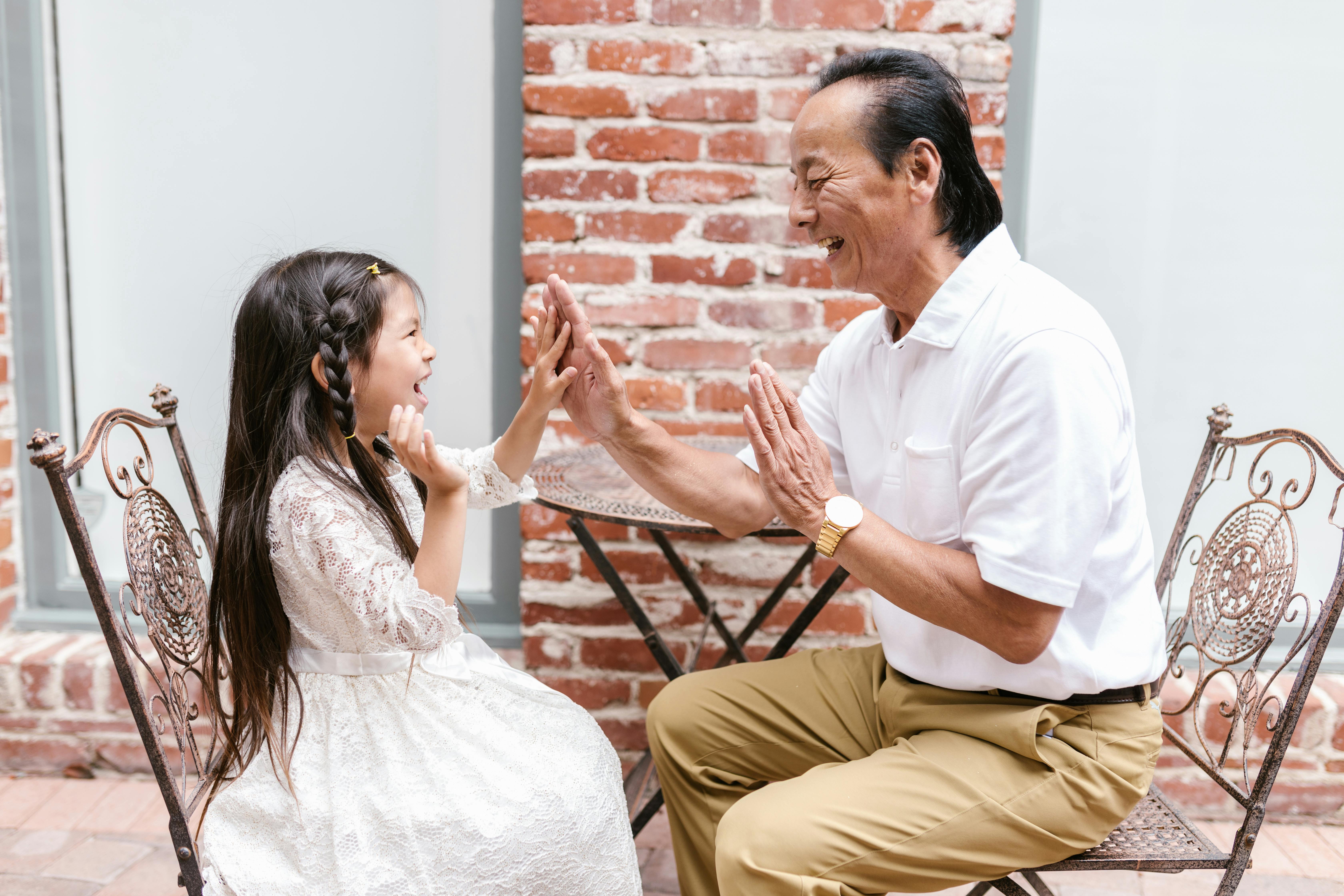 An Asian grandparent high-fiving his granddaughter with a joyful expression