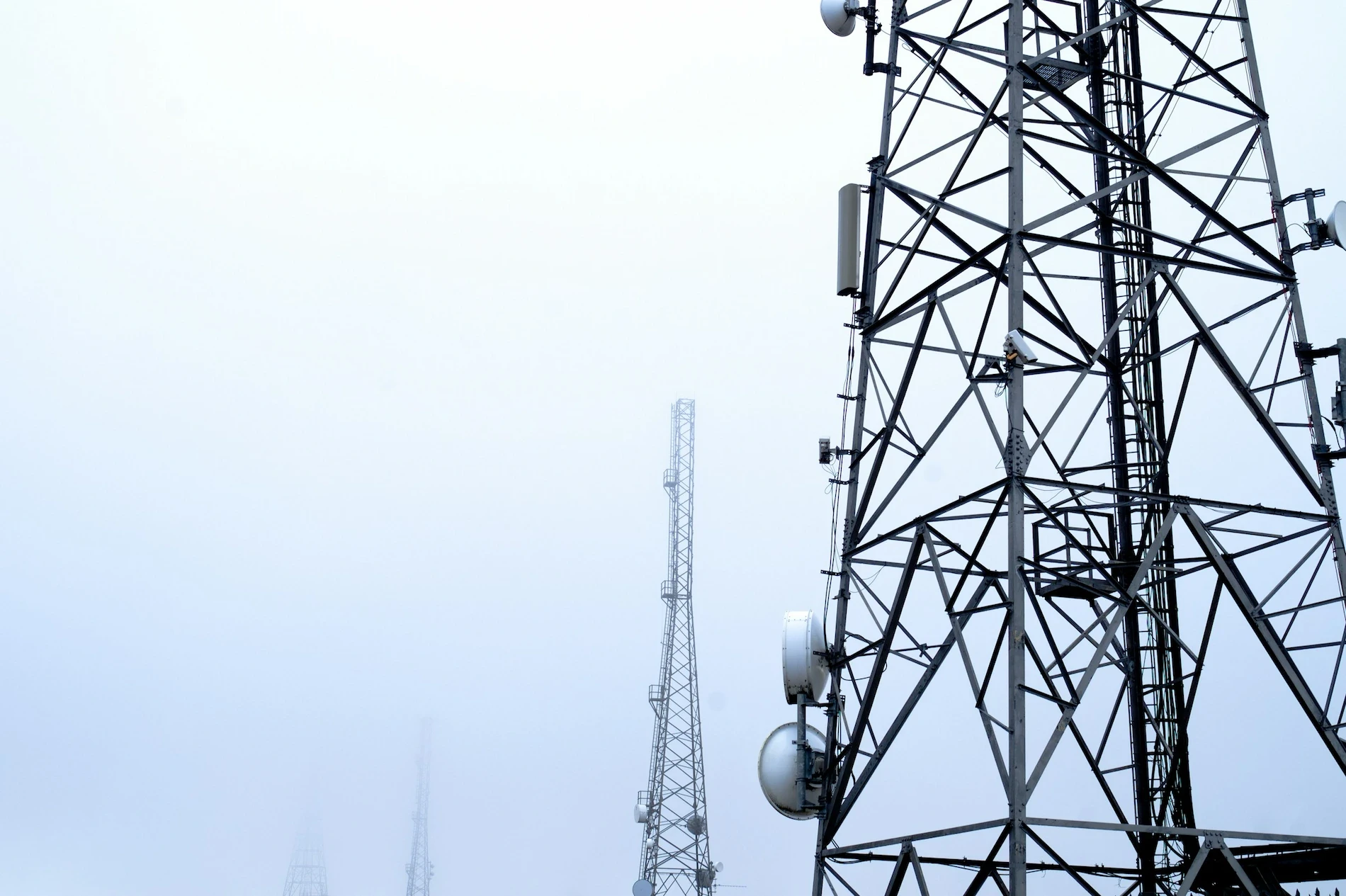 Steel lattice radio towers with microwave dishes appearing through a foggy landscape, highlighting structural details