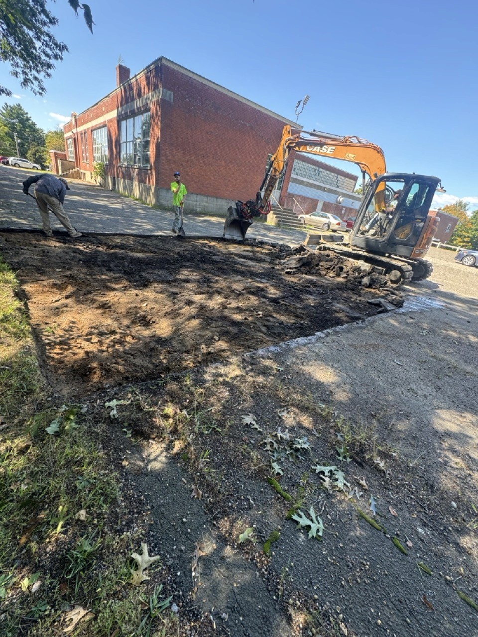 Excavator stripping sod beside a school building