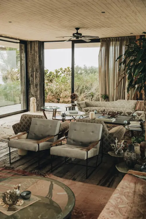 Interior view of Casa Sastran living room with exterior greenery, sofas, and armchairs.