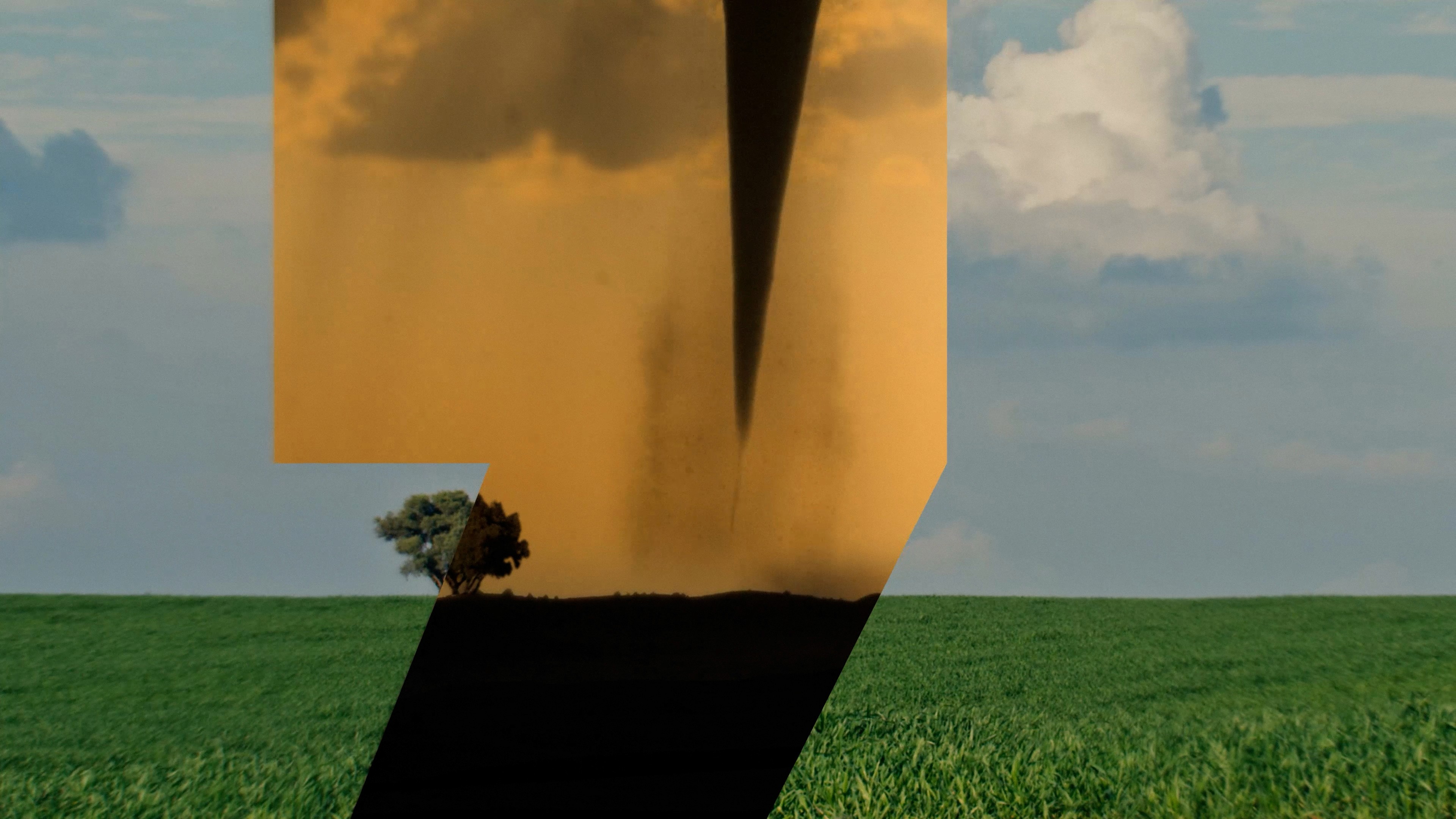 Composited footage of a green field and a tornado approaching a tree
