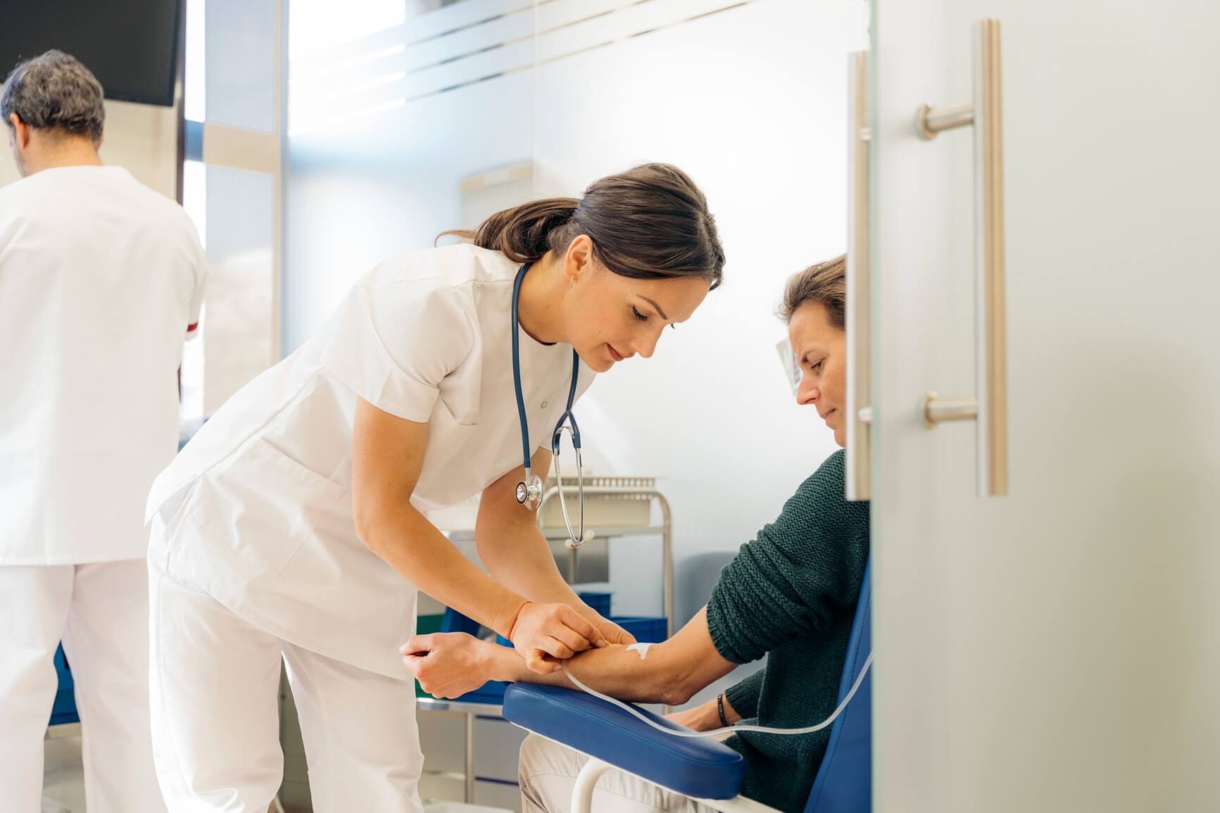 Healthcare worker inserting a needle into a seated patient’s arm in a medical clinic.
