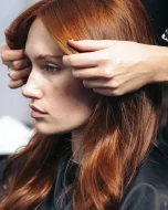 A person styling the hair of a copper coloured model.