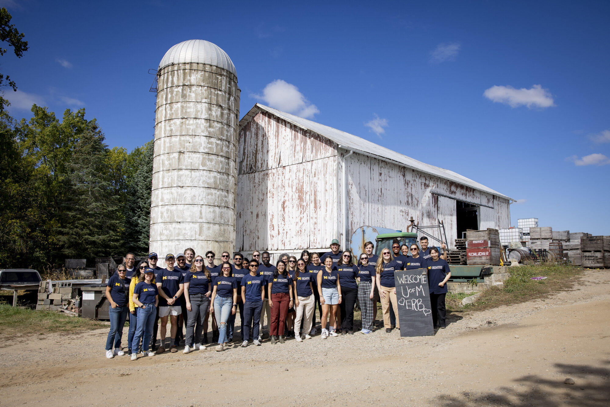 A large group of people poses in front of a barn under a clear blue sky.