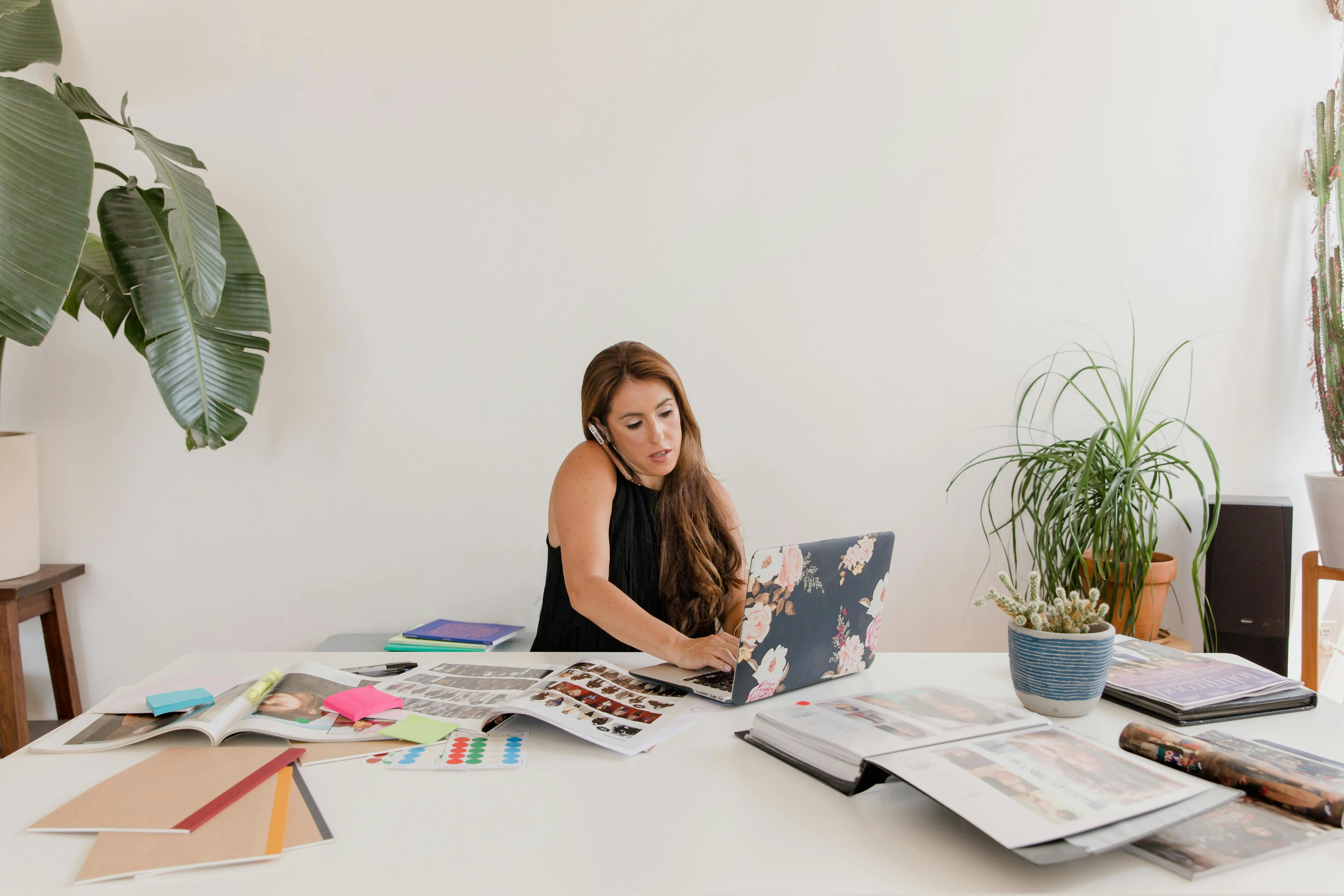 An interior designer uses a laptop and digital tools at a bright workspace to integrate AI-driven workflows into her creative design process.