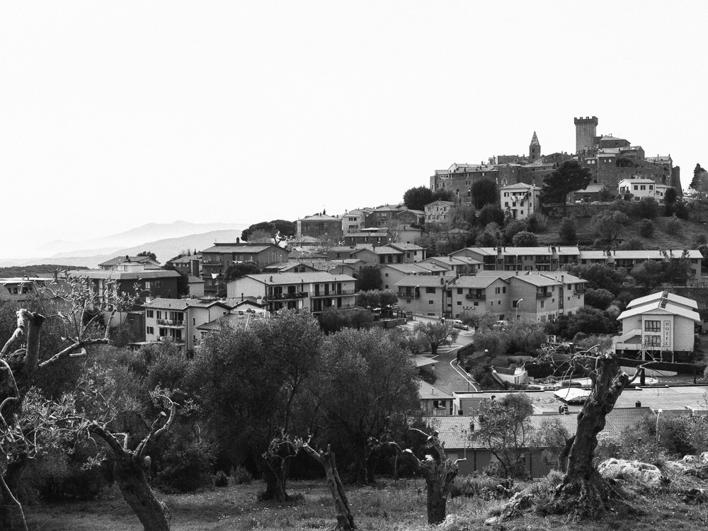 A black-and-white photo of a hilly landscape with scattered buildings and trees.