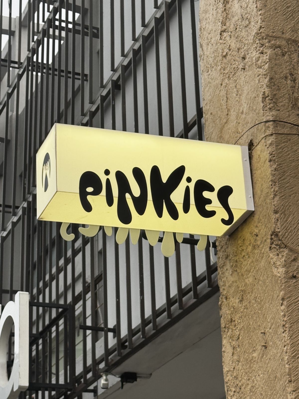 Illuminated “Pinkies” blade sign mounted on exterior café storefront.