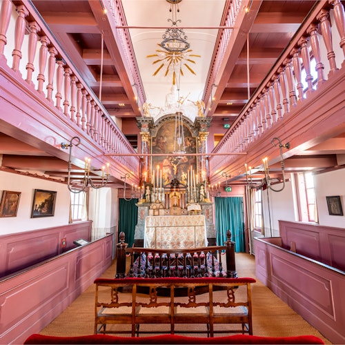 一個裝飾華麗的教堂內部,中央祭壇上方懸掛著華麗的吊燈,兩層粉紅色的圍欄和一排排的長椅。