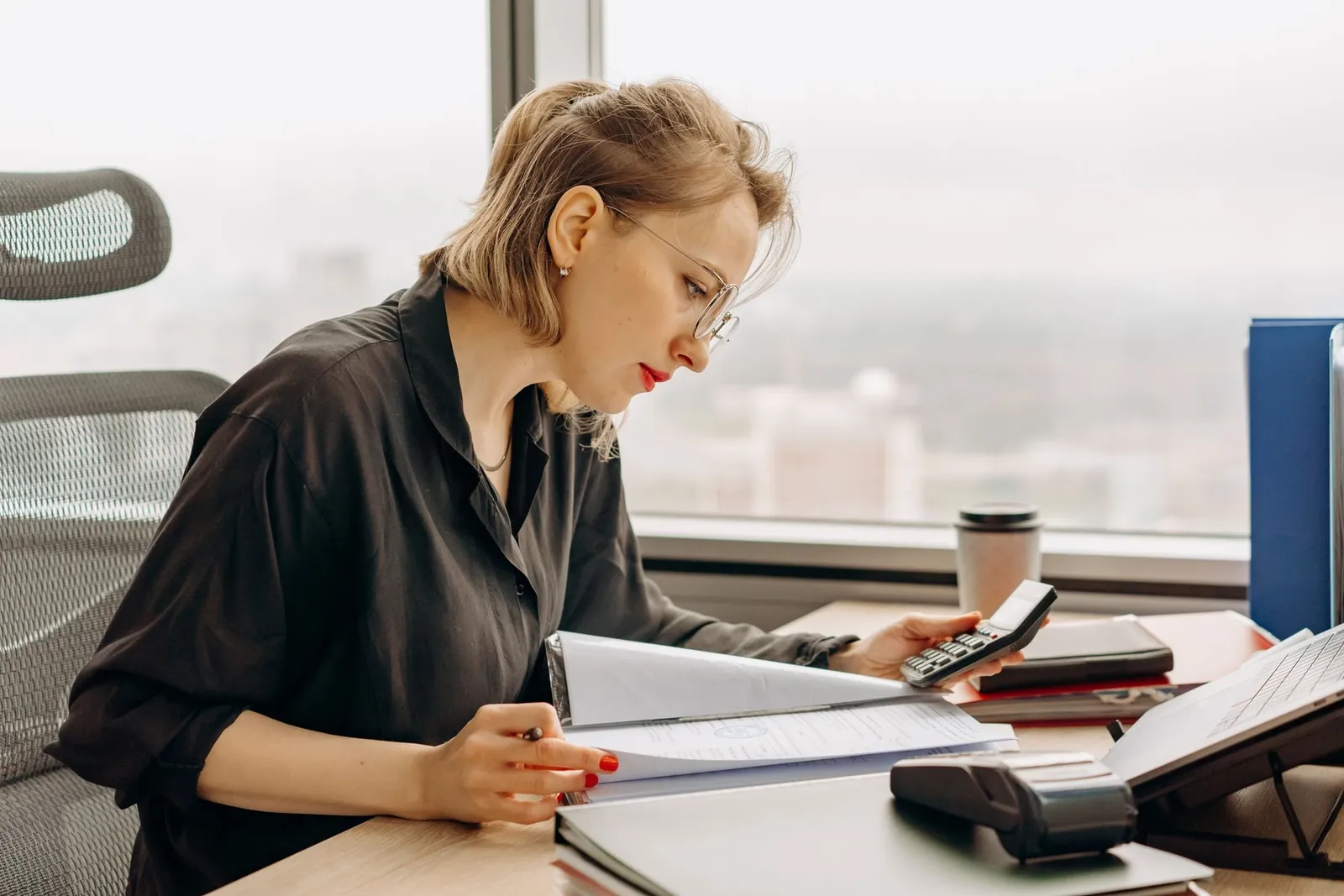 A woman working through financial documents with a calculator at her desk