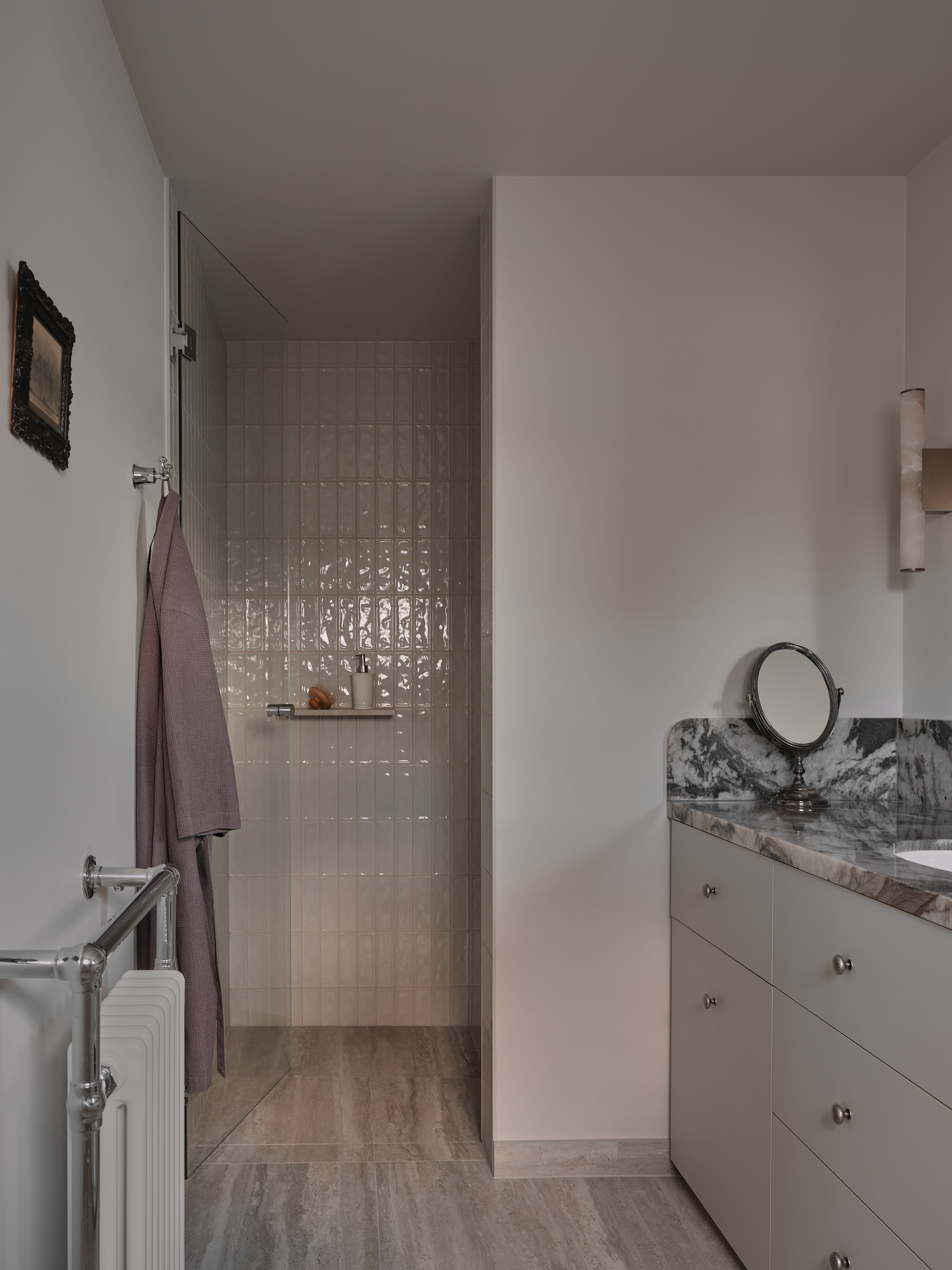 Shower area with textured glass partition, chrome heated towel rail, and ceramic floor tiles