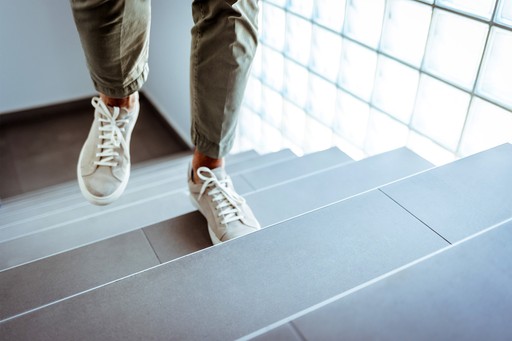 Person mit hellen Sneakern und hochgekrempelten olivgrünen Hosen läuft eine moderne Treppe hinauf