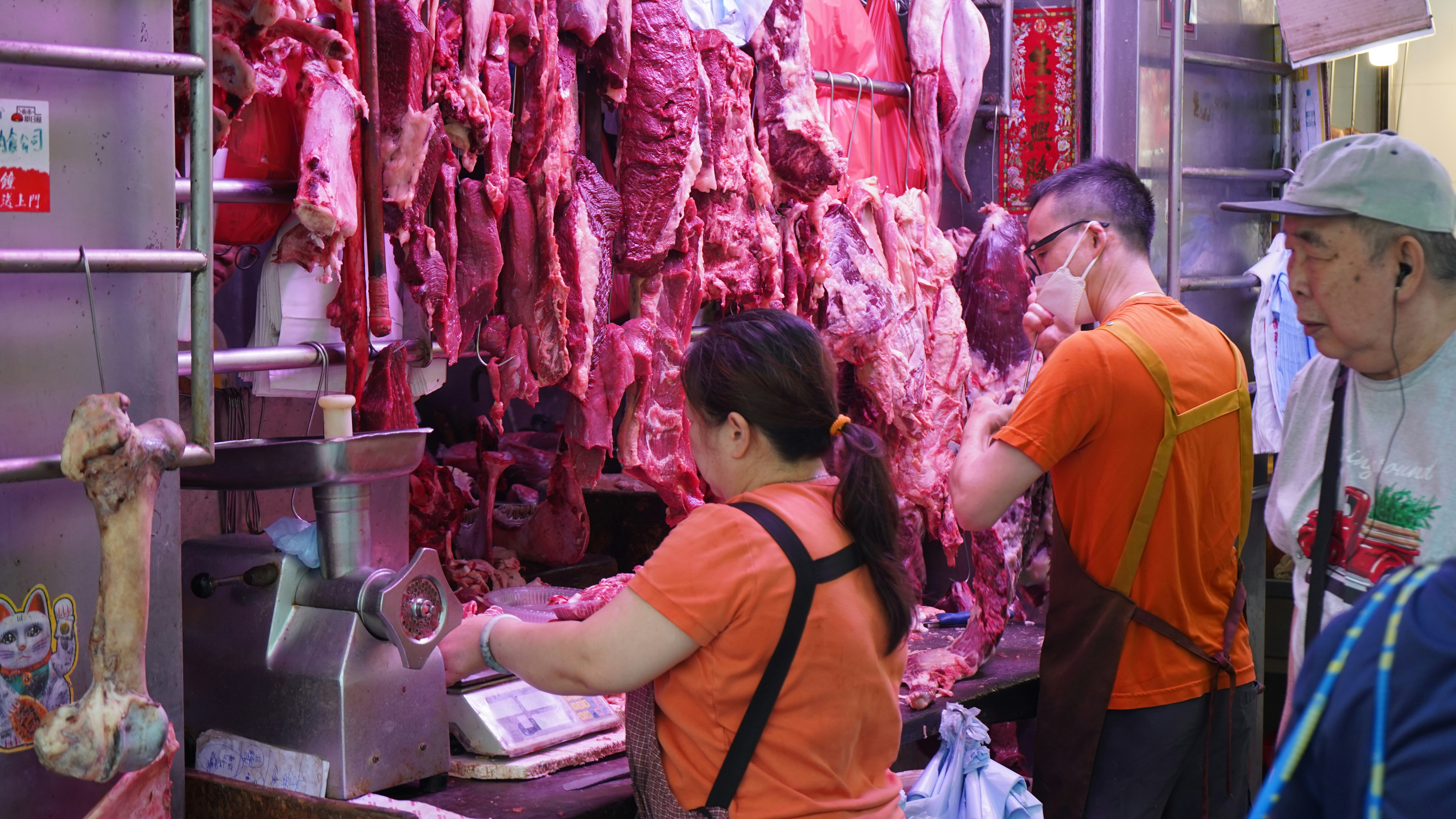 Butchers working at a meat stall with hanging carcasses.