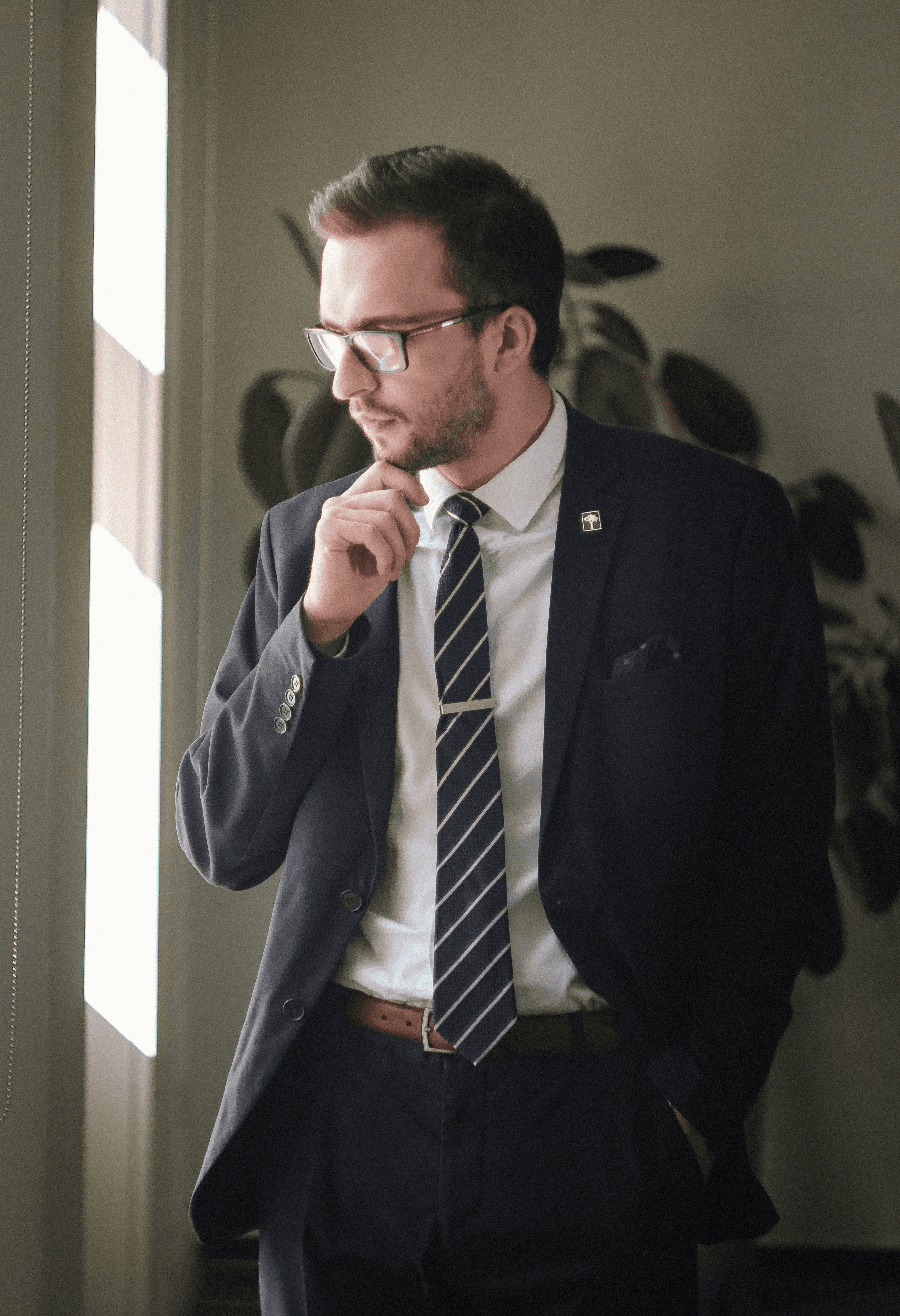 a man in a suit and tie standing in front of a window