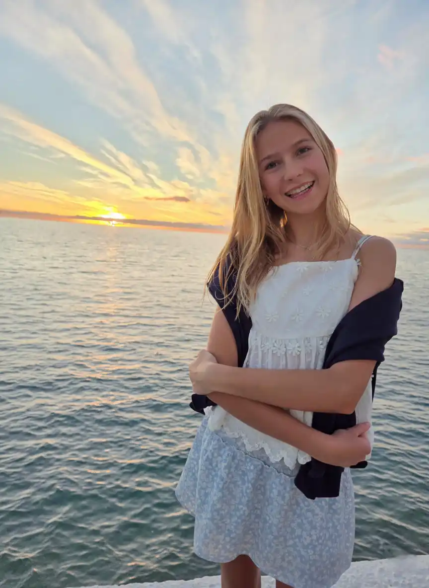 Smilende jente foran en solnedgang ved havet.