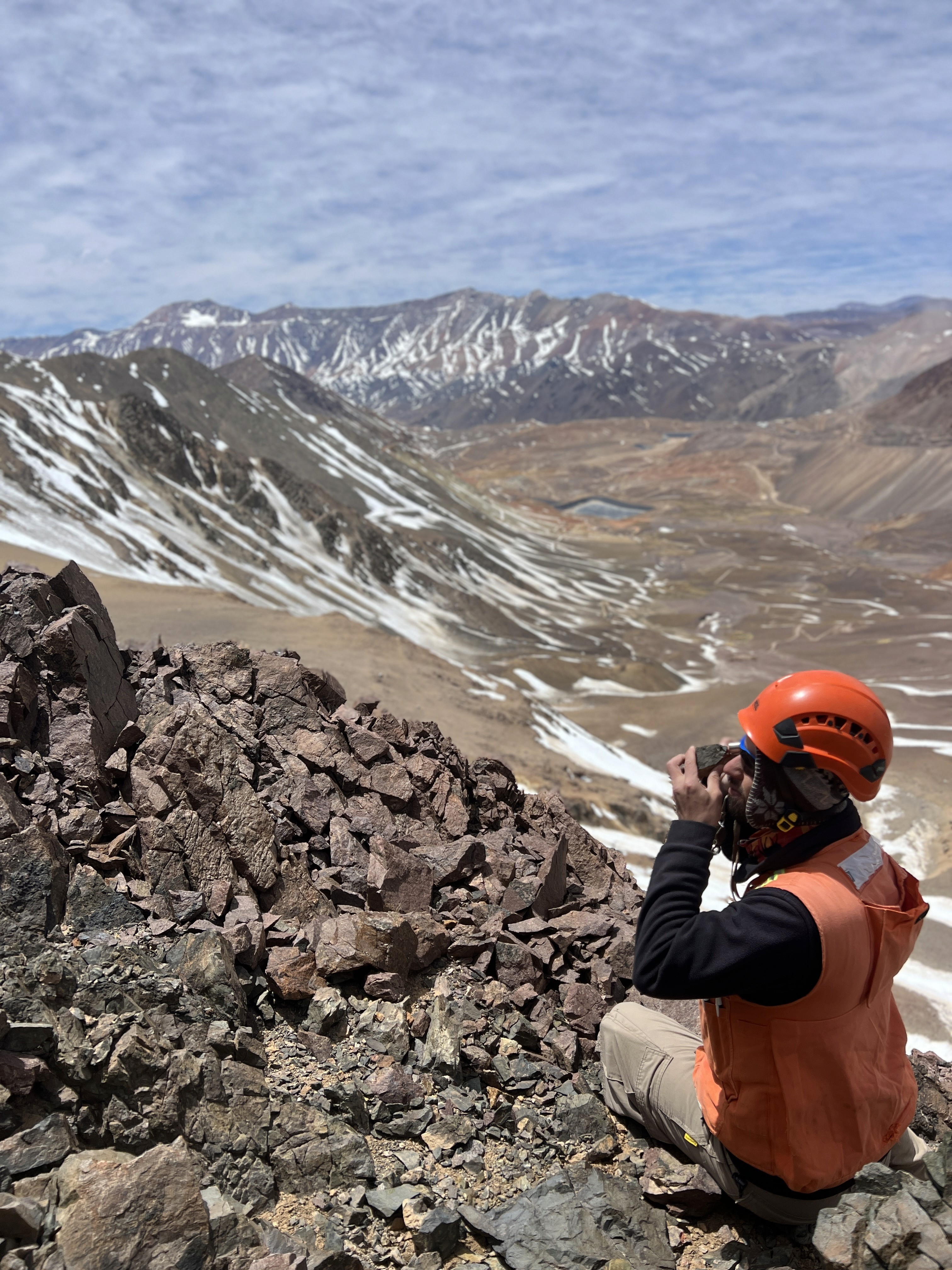 Un geólogo observando una muestra con su lupa y de fondo un valle desértico con algo de nieve